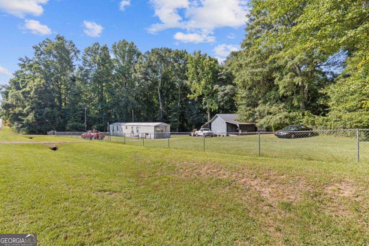 Now eligible for cash, conventional/FHA/VA financing. This mobile home, situated on a level and fully fenced 0.63-acre lot, presents a fantastic opportunity for a small family residence, roommate rental setup, or investment property-whether for rental income or future land development. The home features an open-concept floor plan combining the living room, dining area, and kitchen, creating a welcoming and functional living space. On one side, you'll find a spacious bedroom with an en-suite bathroom, while the opposite end of the home boasts an even larger master-style suite, offering privacy and comfort. All major appliances, including the washer and dryer, are included with the sale. The property also features a separate outbuilding with two attached pole barns-ideal for additional storage or covered parking. Enjoy the benefits of a private well (no monthly water bill) and a recently serviced septic system, both in excellent working condition. The expansive front and back yards are fully fenced, making it perfect for pets or outdoor activities. This cozy and comfortable home is move-in ready, with plenty of potential to personalize or enhance further.