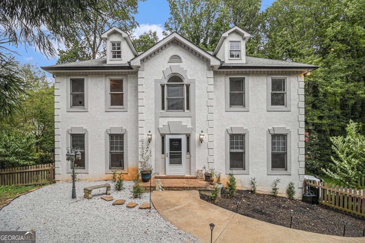 This charming traditional two-story home with a finished basement and three-car parking (including a rare tandem garage) is tucked away on a beautifully landscaped lot, offering a perfect blend of space, privacy, and convenience. The fenced front yard and wooded backyard views provide a peaceful, private setting that's hard to find. Step inside to a freshly painted interior showcasing crown molding, wainscoting, gleaming hardwood floors, and new light fixtures throughout. The formal living room and formal dining room set an elegant tone, while the inviting family room features a tray ceiling, beautifully stained built-ins flanking a classic fireplace, ad great natural light creating the perfect gathering space. The eat-in kitchen offers granite countertops, travertine backsplash, breakfast bar, along with access to the back deck for easy outdoor dining. Upstairs, the vaulted primary suite is a spacious retreat with tray ceilings, a soaking tub, walk-in shower, double vanity, and a generous walk-in closet. Three spacious secondary bedrooms, and an additional full bath accommodates guests or family with ease. The finished basement provides incredible flexibility with a media room, or potential home gym, office, or playroom-ready to suit your needs. Outside, enjoy a backyard filled with apple, pear, fig, nectarine, peach, mulberry, apricot trees, and grapes, offering a mini orchard right at home. With leaf guard gutters, a new hot water heater, and thoughtful upgrades throughout, this home is move-in ready. NO HOA allows you to design and customize you outdoor living based on your lifestyle. Located just minutes from Kennesaw State University, top-rated schools, healthcare, shopping, dining, and major highways, this home combines classic charm with modern convenience in one of the area's most desirable locations. Don't miss this one-of-a-kind opportunity!