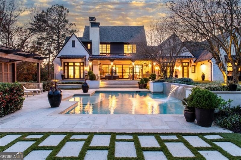 Set on one of the most beautiful lots in one of Atlanta's most desirable neighborhoods, this custom-built home by Mike Hammersmith blends classic architecture with refined, modern living skillfully curated by Greg Busch as featured in Atlanta Homes & Lifestyle magazine. As an early trendsetter, the painted antique brick fa ade, steep gables, and gas lanterns make a striking first impression, while the circular drive and pristine landscaping signal a home that's both luxurious and inviting. Inside, clean lines, natural textures, and expansive steel windows and doors create a light-filled, airy atmosphere. From the moment you enter, enjoy only the finest of details. The main living space is anchored by a dramatic stone fireplace and opens seamlessly to a chef's kitchen outfitted with top-tier appliances, custom cabinetry, and an oversized island made for gatherings. The adjoining dining room is framed by oversized windows and artful lighting, perfect for elegant entertaining or casual family dinners. Tucked off the main living area is a relaxed keeping room mixed with shiplap and exposed brick that adds space to unwind or entertain with built-in banquette seating. Ideal for laid-back meals, morning coffee and relaxation surrounded by the serene landscape. There's also a thoughtfully designed private study with custom built-ins and a quiet, inspiring vibe with a hidden door leading to the primary suite. Other main floor features include a stylish powder room, a private work nook or homework station, and a fully built-out mudroom with locker-style storage and a pool-ready changing hall just steps from the backyard. The primary suite on the main level is a private sanctuary with terrace access, a spa-style bath with dual vanities, marble shower, and a soaking tub positioned under soft natural light. Every finish-from the herringbone tile to the custom built-ins-has been chosen with quiet luxury in mind. Upstairs, four generously sized en suite bedrooms provide comfort and flexibility for family or guests. Each space is thoughtfully designed with walk-in closets, designer bathrooms, and plenty of natural light. A central loft adds a flexible space for homework, lounging, or gaming-whatever fits your lifestyle. A second laundry room upstairs adds convenience without compromise. The terrace level offers a full media room with exposed brick and industrial flair, plus a stylish kitchenette, an expansive rec room, gym, stage, hidden play lounge for the littles, bonus storage, third laundry room, and wine cellar potential-all perfect for entertaining, weekend sleepovers, or long-term visitors. The outdoor spaces are as intentional as the interiors-built for year-round enjoyment and effortless entertaining. A covered patio serves as an all-season extension of the home, complete with a cozy fireplace, TV, built-in heaters, and a full outdoor kitchen. Just off the patio, a dedicated dining area invites long alfresco meals and easy gatherings. The resort-style pool takes center stage, with serene water features, tanning ledges, and multiple lounge areas that feel more like a boutique retreat than a backyard. A shaded cabana offers additional space to relax, unwind, or host guests in comfort. Surrounding it all is mature, thoughtfully planned landscaping and a level turf lawn-ideal for play, pets, or simply enjoying the view. The wooded backdrop provides privacy and a peaceful connection to nature, elevating the outdoor experience into something truly special. Every inch of this home has been curated with intention-from layout to lighting, indoor spaces to outdoor escapes. It's more than move-in ready. It's built for the way you live.