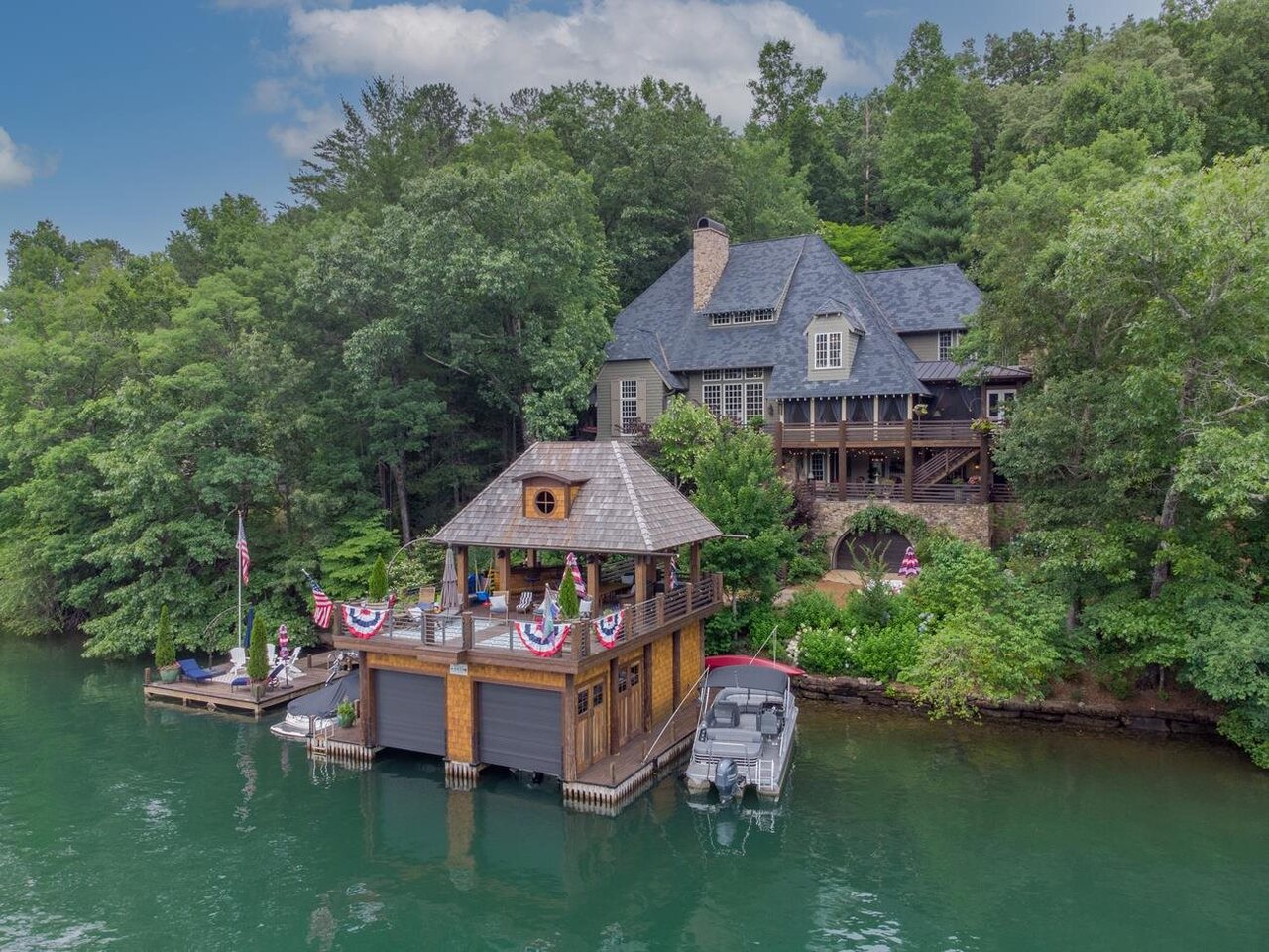 This 6 bedroom, 6 full and 2 half bath Bobby McAlpine designed home features mountain sunset views down Dick's Creek cove from a new 2-story boathouse. A spacious living room and dining area with white shiplap walls and ceilings overlooks lake views. A 2-story stacked stone wall houses an oversized masonry fireplace. The chef's kitchen features antique beams, a custom built island with walnut top, subzero refrigeration, 2 sinks, a double oven, 6-burner gas cooktop, under counter ice maker, standard dishwasher plus a set of dishwasher drawers. A walk-in pantry and appliance closet houses a coffee bar with plenty of well-organized storage space. Antique French doors lead to screened porch overlooking the lake with a stone fireplace, lounging area, dining area and access to a grilling deck. A beautifully landscaped waterfall off the porch drowns out any outside noise creating a truly serene environment. The private owner's wing offers separate walk-in closets; en-suite bath with separate vanities, water closet, jetted tub and separate tiled shower. The master bedroom features tall ceilings with flush mount antique beams, a masonry fireplace with gas logs flanked by built-in bookcases and access to lakeside balcony. Upstairs, a private guest suite offers a wall of windows showing off water views through a canopy of trees. An en-suite secondary sleeping room provides space for extra guests. A full bath includes a jetted tub, separate shower, walk-in closet and water closet. An office with lake views features a full bath and could be used as a bedroom. The office accesses stairs leading to a 3rd floor playroom with a bunk room and full bath. The terrace level features a generous family room with masonry fireplace surrounded by pecky Cyprus and arched windows showing off lake views. A wet bar with under counter fridge and icemaker is conveniently located by the wine cellar. A private guest suite features white shiplap walls, lake views, access to a lakeside porch and a full bath with separate vanities, jetted tub, separate shower and water closet. A second terrace level guest bedroom offers lake views, a private full bath and walk-in closet. A terrace level covered porch features an outdoor fireplace overlooking the lake. A lower-level workshop is accessible from a hidden spiral staircase in a terrace level bedroom with a garage door that opens to the lakefront. This space could be converted to a rec room or outdoor kitchen area to service the boathouse. Lush landscaping and 2 waterfalls surround the home with seating areas nestled into the landscape to enjoy the grounds. A newly built 2-story boathouse on deep water includes a bar with under-counter fridge, dining area, lounging area and beautiful mountain and sunset views down Dicks Creek.