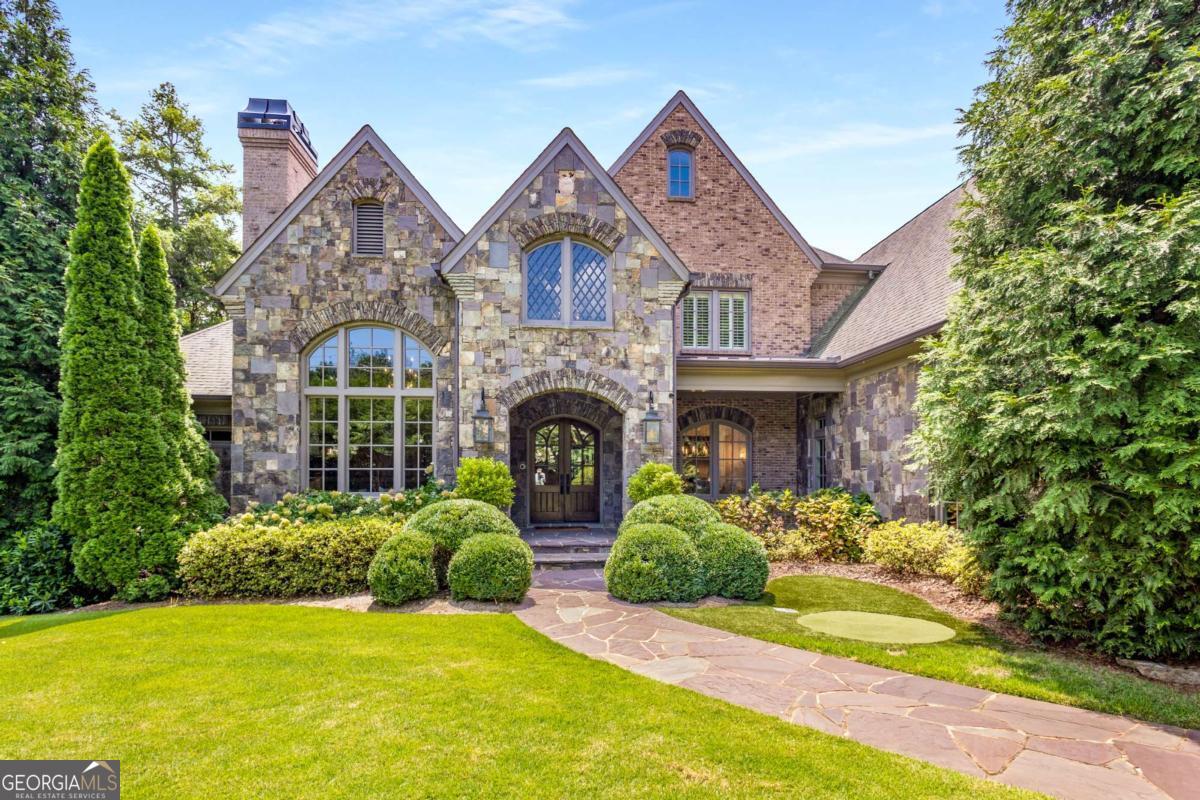 English Manor Estate custom built in 2009 by North Atlanta Properties minutes from Chastain Park in the heart of Sandy Springs, proudly boasting approx. 13,000 sq ft of thoughtfully designed space. This luxury brick and stone home is graciously sited on a 3/4 acre corner lot, behind layers of lush landscaping and a solid brick privacy wall, completely hidden from street view. As you pull in through the solid steel and mahogany automatic car gate onto the interlocking paver driveway, you are taken aback by the incredible landscaping that fully envelopes this lot. Step inside and see the perfect combination of modern conveniences with an elevated old world style! Walls of custom iron doors/windows, exposed brick and stone archways, gas lanterns, stained tongue & groove wood ceilings, Palladian windows, Brazilian Mahogany French Doors, rough hewn beams and more! Handsome main level study features 16' coffered ceilings, herringbone floors, hand carved stained cherry paneled walls, fireplace with custom mantle with marble surround + grand Palladium window. Formal dining room with custom trim, trey ceilings and is open to the formal living room with built-in bookcases and a custom hand-carved limestone mantle. One of a kind kitchen features professional grade appliances, furniture style cabinetry, double dishwashers, multiple ovens, warming drawer, refrigerator drawers, pot filler, huge island + separate professional chef scullery! The kitchen flows naturally through classic brick and stone archways to the breakfast room and large family room w/built in book shelves and fireplace. Temperature controlled 300+ bottle wine room and Butlers Pantry w/ice maker! Mud Room, Home Management/Office center and loads of storage throughout. Primary on main features a double trey ceiling with rope lighting, floor to ceiling box bay window and custom iron doors! Spa bath features heated tile floors, air jet soaking tub, steam shower with multiple heads and plenty of storage throughout. Primary closet has two distinct areas with custom built-in shelving and center island. With multiple living spaces, each offering their unique experience, this home can accommodate casual get togethers to formal dinners of 100+! The Sellers created a tremendous custom living space curated by the great Bill Harrison. Accessed through multiple areas of the home through custom iron doors, this space is pure zen. The entire back wall is comprised of custom, floor-to-ceiling, power iron windows that are operated by remote control. This jewel box of a room also features a custom two level clear-story which allows for natural light to flow from every direction! 5 generous guest bedroom suites and bonus room upstairs. Huge walk up attic with permanent stairs for additional storage! The finished terrace level doesn't disappoint. Large home gym, theater, built-in custom wet bar, private guest suite, two full bathrooms, billiards room, fireside den, dining area and enclosed flex lounge/entertainment space! The backyard is an oasis in the city! Professionally landscaped offering manicured privacy and featuring a heated Pebbletec saltwater pool with waterfall, heated spa + patio of Pennsylvania Lilac stone & custom outdoor fireplace. Sited on a corner lot which provide sidewalks + special turning lane for easy ingress/egress, walking & safe on street parking for guests. Whole house generator, Control4, putting green and loads of extras - Welcome Home!