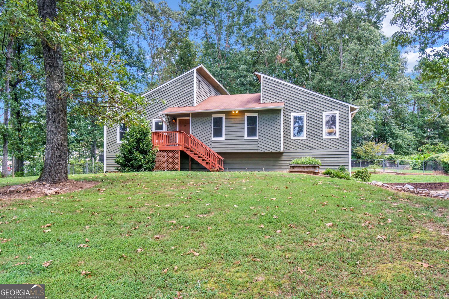 Come discover this lovely, contemporary retreat in an unbeatable location: 1797 Kelvin Drive is a unique raised ranch in the heart of Gwinnett County. This desirable neighborhood is located just minutes from I-85, GA-316, the Mall of Georgia, The Exchange at Gwinnett, Rock Springs Park, and downtown Lawrenceville's shops, restaurants, and cultural venues. Inside, you will enjoy the vaulted family room with its charming stone fireplace, parquet hardwoods, and custom built-ins. The kitchen features abundant and freshly painted cabinetry, newer stainless steel appliances, and a window that frames the view of the lush rear yard. Step out to the private deck and experience the peace of your own backyard oasis. The spacious primary suite includes a private bath and a separate dressing area, while two additional bedrooms share a freshly painted hall bath. Downstairs, the partially-finished basement provides ample storage, a large laundry room, and flexible living space with a broadcast-quality recording studio. This incredible feature is a 6x9 pro isolation booth finished with panels of Owens-Corning 703 acoustic fiberglass insulation which was designed by an acoustician. Vocal artists and musicians will appreciate this unique and valuable addition to this wonderful home. The flat, lush yard is truly a hidden gem-fenced and beautifully landscaped with mature trees and expansive greenery that create a sense of serenity. Whether sipping coffee on the deck or gardening in the sun, it provides retreat from the everyday hustle. A large outbuilding adds even more storage for outdoor gear, tools, or weekend projects.
