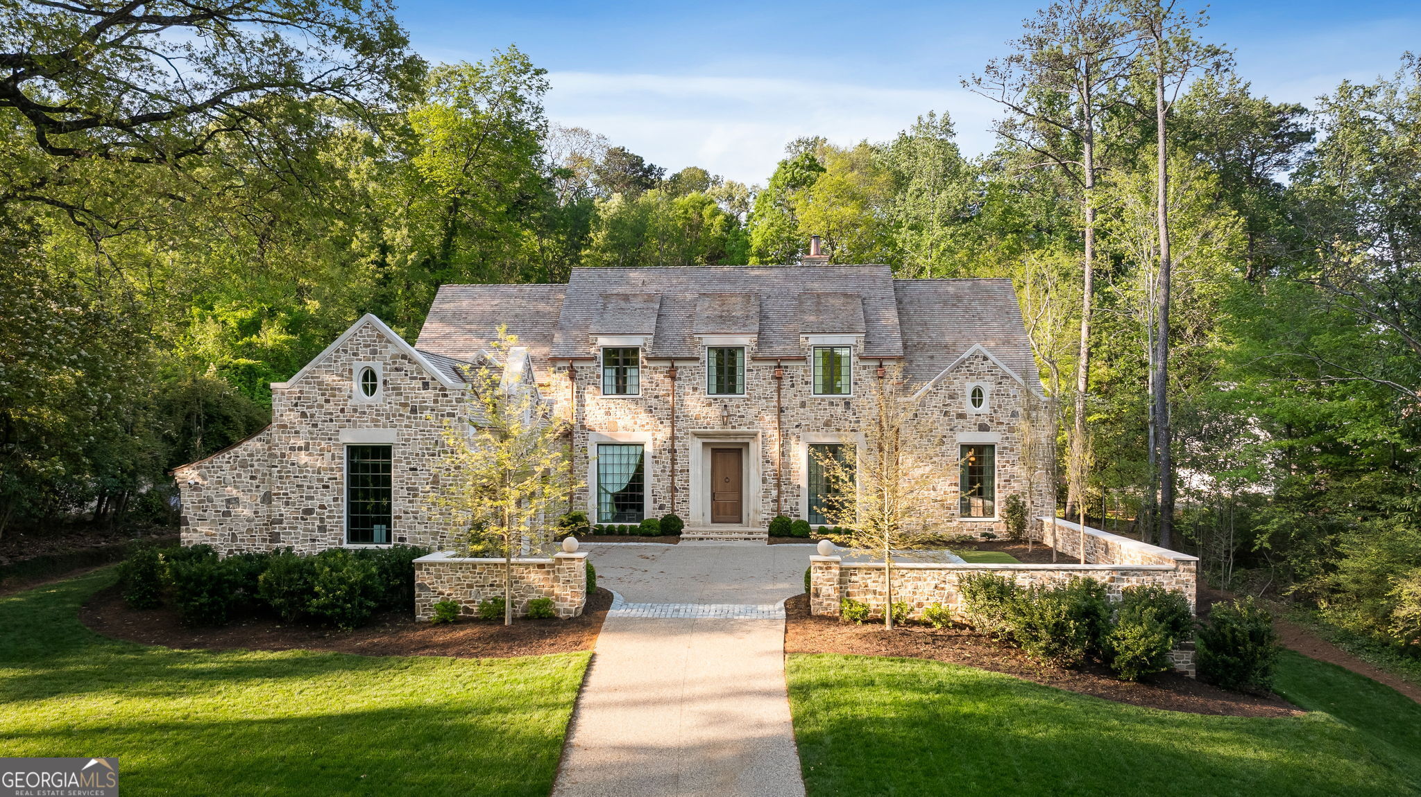Located in the prestigious Tuxedo Park neighborhood of Buckhead, this 7-bedroom estate is a masterful blend of timeless elegance and modern luxury. Designed with exterior architecture by William T. Baker, refined interiors and specifications by SOURCE, and expertly built by Cole Construction, the home evokes the charm of a classic English manor. A striking fieldstone facade, hand-carved limestone accents, and a cedar shake roof lend an inviting, enduring character to this architectural gem. The interior features 12-foot ceilings and blends traditional charm with contemporary flair. Venetian plaster walls, marble accents, and custom wood paneling create an inviting, sophisticated atmosphere. The spacious foyer opens to a cozy living room with a sculpted plaster fireplace and herringbone surround. The chef's kitchen features sleek appliances, brass fixtures, and Kingdom cabinetry, flowing seamlessly into a charming scullery with a checkerboard floor. Decorative plaster ceilings add character to the dining room and primary bedroom, while the primary bath boasts a dramatic barrel arch and a jewel-box freestanding shower. The main-level primary suite also includes dual closets and a spa-like bath. Upstairs, five additional bedrooms, each with marble baths and classic fixtures, offer hotel-like comfort and ample space for family and guests. A playful bunkroom completes the family-friendly layout. The fully finished lower level offers the ultimate in relaxation and convenience, with a media room, bar, gym, sauna, cold plunge, and even a golf simulator. It also features an au-pair suite with a separate entrance, providing privacy and flexibility. The home is equipped with state-of-the-art security, including wired systems and cameras for peace of mind. Phantom speakers are built into the ceilings of the kitchen and family room, and wall speakers are installed on the porch for the perfect soundtrack to any occasion. Outside, the fully fenced backyard is a private oasis with a covered porch featuring a fireplace and stainless-steel gas grill, a sparkling walk-out pool, sports court, and lush landscaping by Land Plus. This estate offers over 1.5 acres of serene, resort-style living, perfect for both relaxation and entertainment.