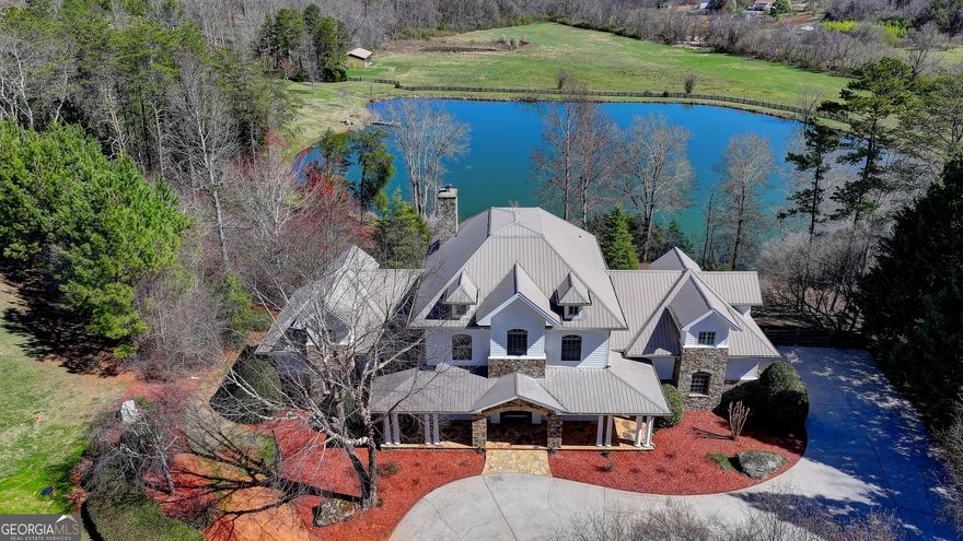 Garden and Gun Dream Home GATED ESTATE on combined 88+ stunning pristine acres with 2 meticulously designed PRIMARY HOMES (6600sf+8,077sf), THIRD RENOVATED GUEST COTTAGE (1800sf approx), separate PRIVATE RECREATION BUILDING/INDOOR GYM, FENCED MAINTAINED PASTURES, and a TROPHY 5-ACRE FISHING LAKE with PRIVATE DOCK. OWNER FINANCE OPTION! 5 Miles from LAKE LANIER. Enter through the stone-gated entrance, where tree lined paved driveway and professional landscaping lead to the main estates, which are privately centered on the property. The stacked-stone covered porch and circular driveway welcome you, with ample parking for guests & events. The professionally designed interior features light neutral tones and a two-story stone fireplace in the great room. Incredible recently designed butler's pantry and coffee/wine bar. The main entrance leads to a library/office with custom furniture grade built-in shelving, a spacious dining room, and a completely remodeled chef's kitchen with Thermador appliance package and sub-zero refrigerator, quartz counters, and new lighting. Expansive windows and balcony french doors offer views of the property and lake. The breakfast room flows into the Great Room with furniture grade built-ins and a flat-screen wiring pkg above the fireplace. The Owner's Suite is on the main level with terrace access, a custom-designed walk-in closet, and a spa-inspired bath with heated floors. The main level includes a perfectly located guest half bath. Upstairs, find four bedrooms and three full baths, including two ensuites. The loft area is customized with bunk beds and offers easy conversion to traditional massive guest suite potential. The upstairs features a spacious private loft seating area lounge. The lower finished terrace level features a custom butcher block island bar, second kitchen, family room, billiards area, 2 full baths, guest ensuite bedroom, and a sliding barn door leading to a massive secure storage discrete fresh air concrete bunker-perfect for a wine cellar, safe storage, or shooting range. The creative possibilities are endless. The lower terrace level opens to a screened porch the entire length of the home, and an infinity custom pool design option overlooking lake. A trex deck and boardwalk lead to the private dock and TROPHY BASS LAKE, designed by Aquatic Environmental Services. The lake is its own ecosystem including investment into Electofish research, 5 feeders, bluegill, crawfish, trout, strain bass, grass carp, as well as a pebble bottom and appropriate aquatic plant life. The property has herds of trophy bucks and deer. The primary estate home includes water purification, fresh air ventilation, and dehumidification. 2nd MAIN RANCH HOME WITH POOL: 7 total ensuite bedrooms and 7 baths featuring an owner's suite with fireplace, Spa inspired bath with soaking tub, tile shower, heated floors, and his/hers custom closets.Woodgrain tiles and new lighting! POOL! Home generator! GUEST COTTAGE: A 2-bed, 2-bath caretaker or guest suite cottage with private driveway and views, covered front porch and spacious accommodations overlooking large pasture. PRIVATE GYM REC BUILDING: Features a basketball/pickleball court, golf simulator room, kitchen, and two bathrooms with spaces for exterior expansion ideas like tennis or outdoor rec/barn. The land features fenced pastures and a smaller pond ideal for a home site, barn, equestrian facilities, gardens, or homesteading. There is a chicken coop! What is your vision? The estate is close to Lake Lanier, private airports, Falcon Training Camp, UGA campus, wineries, vineyards and more. The driveway provides easement to a neighboring 52-acre estate that is also on market with different office, for those interested in a combined 88+ acre compound. Call today for an appointment. We are here to help! Be sure to interact with the virtual tour here! (2 estates sold as combined or individually, call for details).