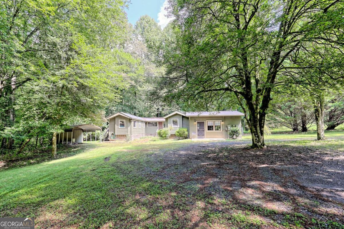 Looking for an affordable getaway? Check out this unique property featuring two cedar-sided park models, each with one bedroom, built-in cabinetry, a bathroom, separate kitchens with eat-in areas, and a small den. Both units connect to a spacious stick-built den with a wall of windows and access to two separate decks. An additional family room for extra living space, along with a separate laundry room, provides additional storage. The property includes a single carport equipped with electrical outlets and a storage room with lighting, PLUS an additional storage shed, which also features lighting. There's also a small fenced area for your pets and an RV electrical hookup. You can often hear the Syrup Mill Creek from the decks that border the back of the property. The property backs up to the 8th hole of Mountain Harbour Golf Course, enhancing its privacy. The level lot has a circular driveway for easy access and ample space to park your boat or extra vehicles. With some trimming, the established blueberry bushes will give you a bountiful harvest of delicious NC blueberries. Stay connected with fiber optic internet from BRMEMC, providing superior quality for TV streaming. Situated just minutes from Lake Chatuge, Ingles, and the Square in Hayesville, this 0.66-acre lot is an excellent opportunity for rental investors or your personal retreat, with no HOA fees and minimal yard maintenance. Don't miss this opportunity!