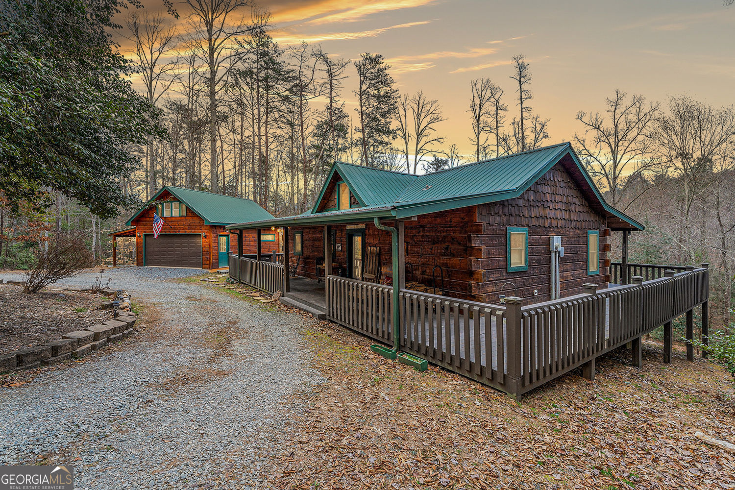 Set on 2.2 private acres in the scenic Blue Ridge Mountains, this single-story log cabin delivers a true mountain retreat with room to stretch out and slow down. A circular drive winds under a canopy of mature hardwoods, leading you to a home where the pace feels instantly easier. Inside, the kitchen features warm wood cabinetry, coordinating solid-surface counters, and a sunny breakfast nook that opens to a vaulted living room. A floor-to-ceiling stone fireplace anchors the space, perfect for quiet nights or gathering with friends. Two well-sized bedrooms and two full baths offer practical comfort, whether you're here full-time or just on mountain time. The wrap-around porch, complete with an oversized landing, is made for early coffee and evening stargazing, with long-range seasonal views as your backdrop. A fire pit is ready for s'mores and stories, while open grassy stretches invite gardening, games, or simply wandering among the trees. A detached two-car garage keeps vehicles and outdoor gear secure, with the option to finish the space into an additional room or private rental suite. The location puts you near hiking trails, trout streams, and the inviting shops and cafes of downtown Blue Ridge, close enough for convenience, yet far enough to enjoy peace and quiet.