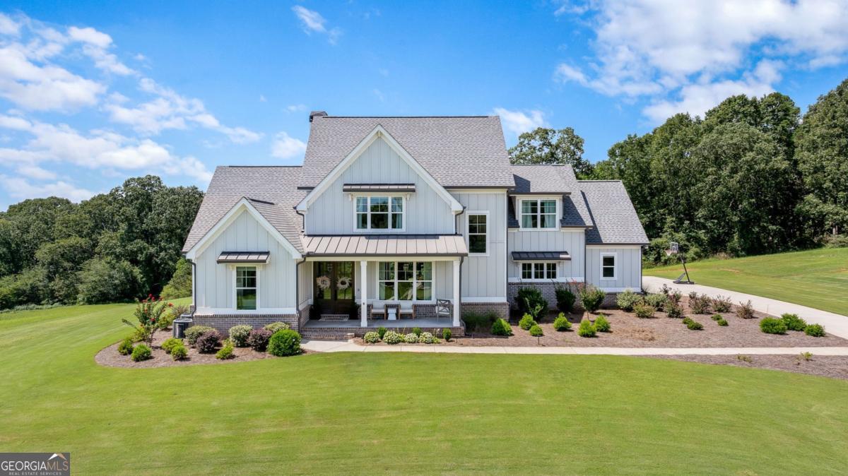 Welcome to this stunning home perfectly situated on 5 private acres within a gated community, offering breathtaking lake views and ultimate privacy. The large covered front porch with stately columns sets the tone for the charm and elegance found throughout. The private owner's suite is conveniently located on the main level, featuring a spa-like bathroom with double vanities, walk-in shower, soaking tub, and private water closet. The gourmet kitchen is designed for entertaining, complete with a spacious island topped with quartz countertops, stainless steel appliances including a gas cooktop, wall oven, microwave, dishwasher, and built-in beverage storage. A walk-in pantry provides ample space to keep everything organized. Enjoy seamless open-concept living with views from the kitchen into the family room, where a beautiful fireplace, custom bookshelves, and access to the covered back patio create the perfect gathering space. Upstairs, you'll find three additional bedrooms plus a finished bonus/bedroom with a full bath-ideal for guests or flex space. This home showcases a high-end trim package and gleaming hardwood floors in the foyer, office, family room, kitchen, and dining area. There is also an option to purchase an additional 5+ acres directly adjacent to the property for those seeking even more space.