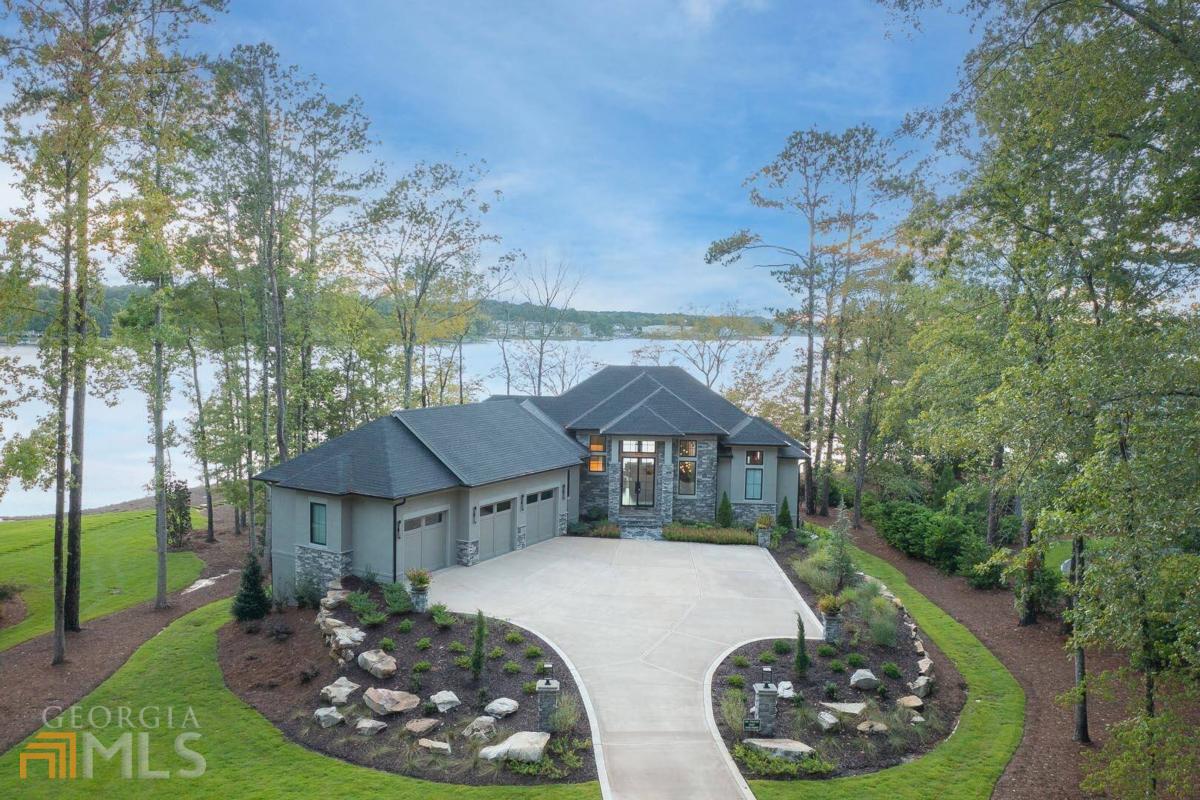 "MODERN LUXURY LAKEFRONT HOME IN REYNOLDS LAKE OCONEE" This breathtaking custom home built in 2021 offers a design aesthetic that makes the most out of lake life while surrounding you with an elegant city feel. The 5-bedroom, 5-bath 4,657 sq ft home sits on a level .97 acre lot with sweeping big water views and privacy in your backyard pool and spa. The home is on a quiet cul-de-sac with an upgraded hardscape package, long driveway, large motor court with entry columns that welcome you to the beautiful property. The custom cast iron front door opens to a striking interior with custom Italian tile flooring, 24-foot ceilings, designer lighting, floating iron and wood staircase highlighted by a custom antique mirrored glass, remote-controlled electric fireplace, 9 ft sliders that open onto a spacious covered porch. The kitchen is framed by Bentley Cambria Quartz waterfall countertop island and coordinating vent hood, sleek custom cabinetry, and professional designer appliance package to include Sub-Zero refrigerator, Wolf cooktop, Cafe Professional Series oven, Cove dishwasher, KitchenAid ice maker and dual refrigerator drawers, and a 288-bottle Zephyr wine refrigerator. The main level hosts the master bedroom and a second bedroom suite that also sets up nicely as an office. Master bedroom has 10" natural hardwood plank floors, remote-controlled electric fireplace, custom Artisan closets, and a master bath with floor-to-ceiling tile throughout, natural wood vanities and cabinets with concrete vessel sinks. Drift downstairs to the terrace level with a wet bar including a KitchenAid refrigerator, Cove dishwasher and quartz countertops. Settle in to watch TV, play a game of pool, or hit the gym with a full bath (fifth bedroom). Two additional bedroom suites with lake views take advantage of the stunning walkout level backyard with a salt water pool/spa with spillway, automatic cover and fire pit. Enjoy the sunset views from the max dock with 7,000 lb boat lift and cover, deep water off the dock for guest boat parking and jet skis. Other features include remote control blinds, high-end bathroom finishes with LED backlit mirrors, large custom seasonal closet, and Smart Home features (security, pool, firepit, door, media, lighting, cameras). Membership is available.