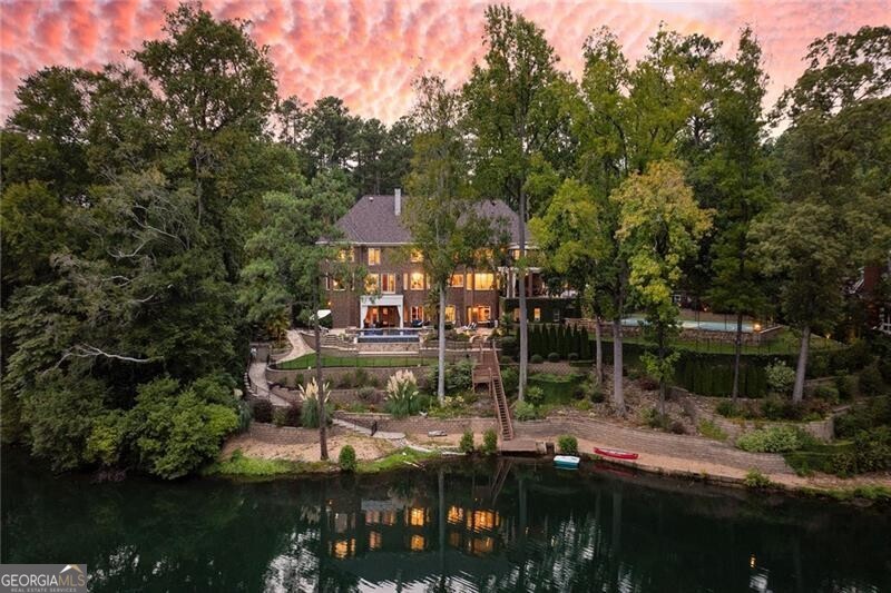 Discover an unparalleled sanctuary with this rare private estate in Sandy Springs, nestled near Chastain Park and Buckhead. Spanning two lush, fully-fenced acres, this exclusive gated property offers breathtaking panoramic lake views that evoke the serene ambiance of Lake Burton, right in the heart of Chastain. Embrace lakeside living with a private dock, a charming paddle boat launch (electric motor boats permitted), and a lakeside entertainment area featuring a bocce ball court, horseshoe pit, and a cozy fire pit. This home is the epitome of luxury and comfort, featuring an elevator that services all levels, a state-of-the-art movie theater for cinematic experiences, and a wine cellar perfect for showcasing your collection. For wellness enthusiasts, there's a workout room, a 12-person sauna, and a private 5-person infrared sauna in the primary suite, along with a steam shower for ultimate relaxation. As you enter the home through the grand, oversized domed foyer, you are immediately welcomed into a main level designed for both elegance and functionality. The open family room seamlessly connects with the kitchen, creating a perfect space for gathering and entertaining. Adjacent to the kitchen, the breakfast room offers a casual dining option with a view. For more formal gatherings, the dining room accommodates at least twelve guests, while an additional covered patio off the kitchen offers another dining alfresco option. This patio can comfortably seat twelve and presents the opportunity to be screened in for year-round enjoyment. The formal sitting room is highlighted by an ornate limestone fireplace, adding a touch of grandeur. The two-story all-wood library or office provides a stunning backdrop for work or relaxation. A versatile bonus room on this level can serve as an additional oversized primary bedroom or a playroom, depending on your needs. Convenience is key with a family entrance located next to the garage entrance, both leading into a well-appointed mudroom. This thoughtful layout ensures that the main level is both practical and inviting, setting the tone for the rest of the home. The second floor is dedicated to luxurious living quarters, with five spacious bedrooms including the expansive primary suite. The primary suite boasts a private patio with a hot tub and a sitting area with a limestone fireplace. The suite's his-and-her closets are remarkably large, with a additional separate closet within for seasonal wardrobe changes. The opulent primary bathroom includes dual vanities, a makeup vanity, a full-sized shower, a separate tub, and an infrared sauna. Each of the additional four bedrooms features an ensuite bathroom and walk-in closet, while the upper-level library offers a tranquil space for reading or card games. The terrace level truly shines as an entertainer's paradise. It features an in-law suite, wine cellar, theater room, pool table room, workout space, massage room, and a 12-person sauna. This level opens to a stunning stone infinity-edge pool overlooking the lake, with a cabana providing a bonus kitchen and bathroom for guests. A sports court adds to the recreational options. This home is a true oasis, perfectly designed for both grand entertaining and cherished family moments. From lakeside fireside games to movie nights, basketball, and pickleball, this residence provides an unparalleled living experience.