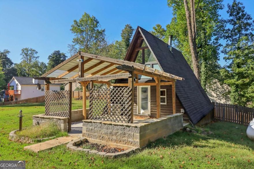 Discover this charming A-frame nestled on a spacious lot just minutes from LAKE LANIER! With no HOA, the possibilities are endless as you're able to design an outdoor space to meet your needs. There's room to add a pool, storage shed, or utilize the ample space for RV/boat parking, and more. The perimeter of the property is fenced, with the option to fully enclose, making it perfect for pets and privacy. The covered front patio adds additional living space for easy indoor-outdoor living. Whether styled with comfortable seating, a mounted TV, or fire pit, it's the ideal place to relax and entertain as cooler weather approaches. Inside, this home exudes COZY RUSTIC CHARACTER with great potential. A NEW SPLIT-UNIT heating and cooling system serves the two-level layout, which features EXPOSED BEAMS, butcher block countertops, a herringbone tile backsplash, and stainless steel appliances. The main level also includes a laundry room with storage and pantry, while the loft offers flexible space for a possible second bedroom, home office, or additional storage. This property is a RARE FIND, whether you're seeking a personal lake getaway, INVESTMENT OR RENTAL PROPERTY. Nearby access to Two Mile Creek Boat Ramp, Bethel Park, Vans Tavern Park, and Pelican Pete's, plus convenient proximity to grocery stores, shopping, and dining. It's the perfect blend of seclusion and accessibility.