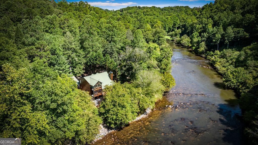 Dreaming of escaping the ordinary & immersing yourself in the mountain life riverside? Whether it's just enjoying the mesmerizing scenes of the glistening Coosawattee River & surrounding native flora & wildlife, splashing in the water, or just relaxing to the sounds of the rushing rapids, this exceptional property offers a unique opportunity to experience outstanding riverfront living. Not only will you appreciate easy access at the waters edge, but you'll also enjoy this lot's gentle terrain, plentiful parking & room to roam. Searching for the perfect space to create moments that matter? This 3 level turnkey riverfront lodge is just the place with room for everyone & a view from each level! The main level showcases an expansive living area with open living room, kitchen & dining all united by soaring ceilings & a warm feeling with the all wood interior accented by the natural light & stone fireplace. The kitchen offers amazing counter & cabinet space, & off this area you'll find the covered deck spanning the backside of the home overlooking the river with steps down to it, as well as pantry, main level bedroom & full bath, & laundry room. Upstairs you'll find the primary ensuite with its own enclosed balcony, soaking tub & separate shower, along with a large loft and an abundance of storage. Moving downstairs, the terrace level was designed with entertainment in mind - an enormous versatile space for your needs complete with a pool table, bunk/hobby space, wet bar, full bath & access to the outdoors where you'll also find the lower level garage. Other unique features include a large 2 level 2 car garage with office and workshop, EV charger, and RV hookup. Located behind the gates of the Coosawattee River Resort with one-of-a-kind amenities, you'll never lack for entertainment, & the access to major travel routes is exceptional for travelers! This home even offers a generator & has been recently stained. Experience the magic of Muller Lane.