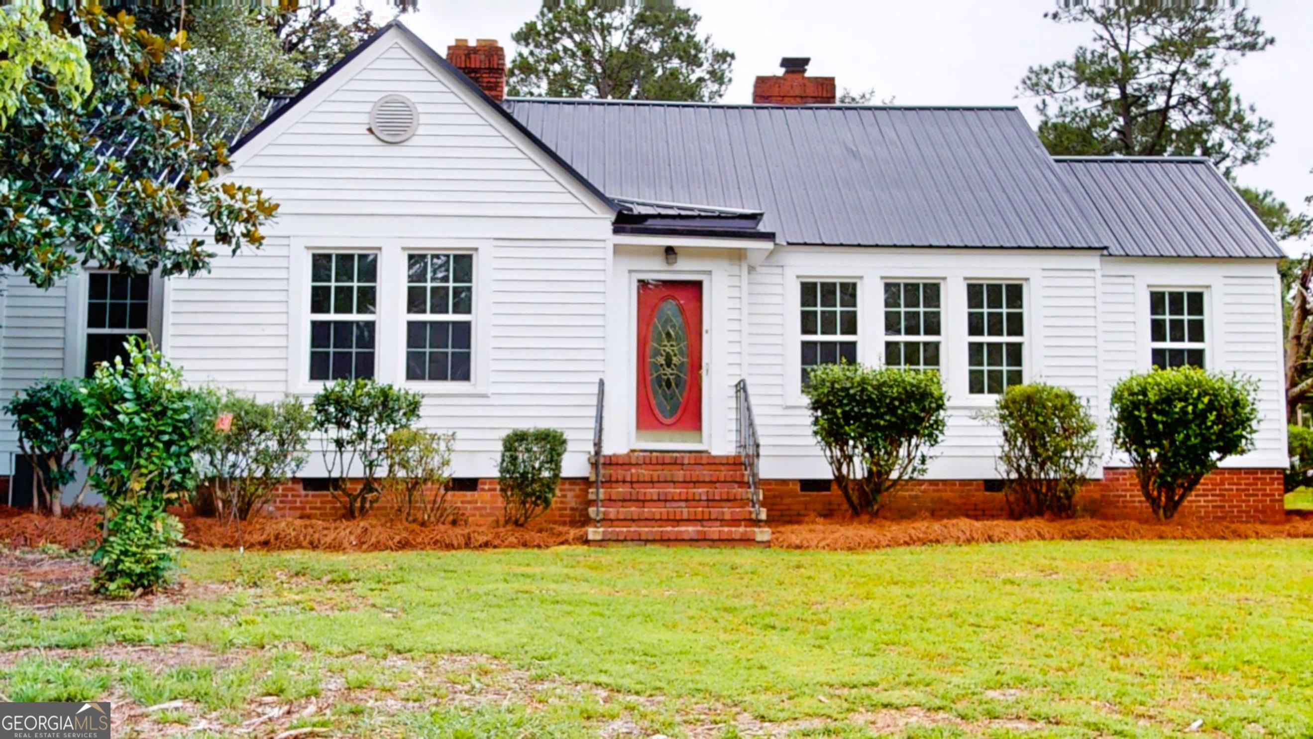 Welcome to this charming 3-bedroom, 1.5-bath home, boasting classic details and comfortable living spaces. Step inside to discover beautiful hardwood floors that extend throughout the main living areas, adding warmth and character to the space. The spacious living room features a classic brick fireplace, perfect for cozy evenings, and built-in shelving, offering ample storage and display space. The bright and inviting kitchen is equipped with white cabinetry, a double sink, and a black range. Plenty of natural light streams in through multiple windows. Each of the three bedrooms features gleaming hardwood floors and generous natural light, creating serene and comfortable retreats. The bathroom includes a corner pedestal sink and a framed mirror. Outside, the home presents a lovely curb appeal with its white siding, dark metal roof, and a welcoming red front door. The front yard is well-maintained, featuring mature landscaping and a lush green lawn. This home offers a fantastic blend of classic charm and comfortable living. Don't miss the opportunity.