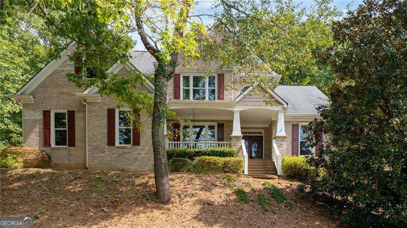 Tucked inside the highly desirable Sweetwater community near Lake Lanier, this spacious home offers exceptional privacy, everyday convenience, and a rare double lot totaling 1.43 acres. Surrounded by mature hardwoods, it provides the perfect blend of seclusion and neighborhood living. From the moment you arrive, the welcoming front porch with a charming swing and double front doors set a warm tone. Step inside to find a formal dining room on the left and a formal living room or office on the right. Continue through to the two-story family room where a wall of windows fills the space with natural light, a classic brick fireplace adds warmth, and hardwood floors flow across the main level. The kitchen features white cabinetry, granite counters, and stainless steel appliances, with open views to the breakfast area and family room so you can cook while staying connected. Host holidays in the separate dining room, and enjoy a quiet, tucked-away main-level office for work or homework. A full guest suite on the main level makes hosting friends and family effortless. Upstairs, the oversized primary suite offers a cozy sitting nook framed by a bay window, tray ceilings, and his-and-hers closets. The bright bath includes two vanities, a separate tub and shower, vaulted ceilings, and abundant natural light. Two additional bedrooms share a full bath, providing ample room for family or guests. The finished basement expands your living space with a full bedroom and bathroom, a second office, playroom, or hobby space, plus a large area ideal for a media room, man cave, or second living room. Outside, a spacious tiered deck overlooks the private wooded lot-perfect for morning coffee, grilling with friends, or enjoying crisp fall evenings. This home is ideally located just minutes from Lake Lanier, Buford Dam Park, and the Chattahoochee River trails, giving buyers easy access to boating, fishing, hiking, swimming beaches, and picnicking. The nearby Laurel Ridge Trail offers a scenic 3.8-mile hike with both lake and river views. The Sweetwater neighborhood enhances the lifestyle with tennis courts, a clubhouse, and beautifully maintained grounds-all within a great school district. With its spacious traditional layout, finished basement, multiple living spaces, and exceptional location, this warm, welcoming property is priced to sell and ready for your personal touch.