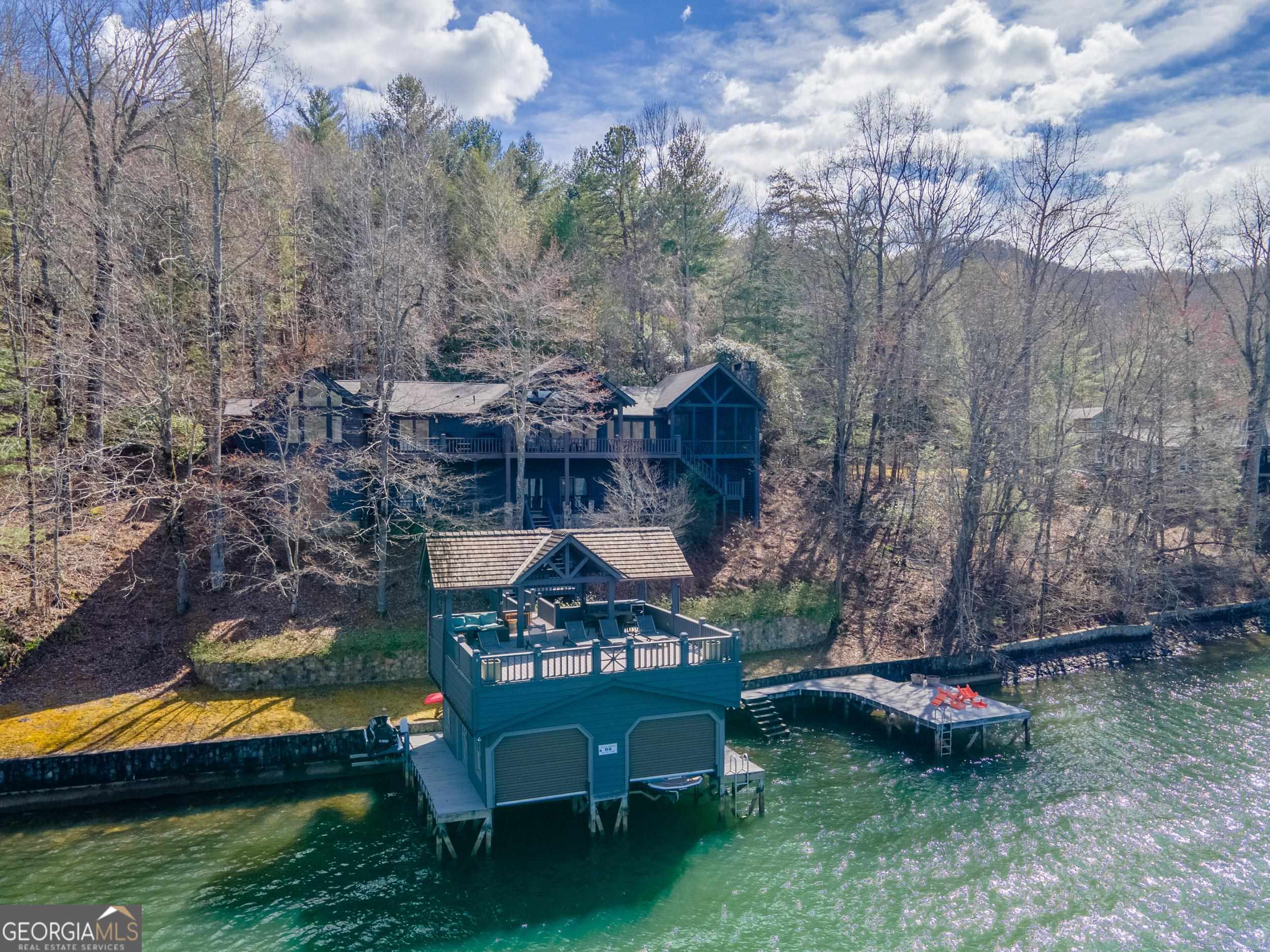 Spectacular Lake Burton Retreat - 4BR, 4BA plus Bunk Room: This classic Lake Burton home epitomizes lakeside living with its panoramic views of Timpson Cove. The open great room features a vaulted ceiling, stone fireplace and French doors leading to a lakeside deck, while the gourmet kitchen, dining room, beverage bar and lakeside screened porch with fireplace offer ideal spaces for entertaining. The main floor boasts an owner's suite with a vaulted ceiling, lake views, fireplace and generous en-suite bath. Two additional guest bedrooms and 2 full baths round out the main floor. The terrace level includes an additional guest bedroom and full bath plus a rec room with built-in bunks and access to a covered lakeside patio. The 2-story boathouse and swim dock are situated on deep water offering long lake, mountain and sunset views. Experience the very best of Lake Burton living in this prime Timpson Cove location, with easy access to Waterfall Club and downtown Clayton. New roof installed in 2024!