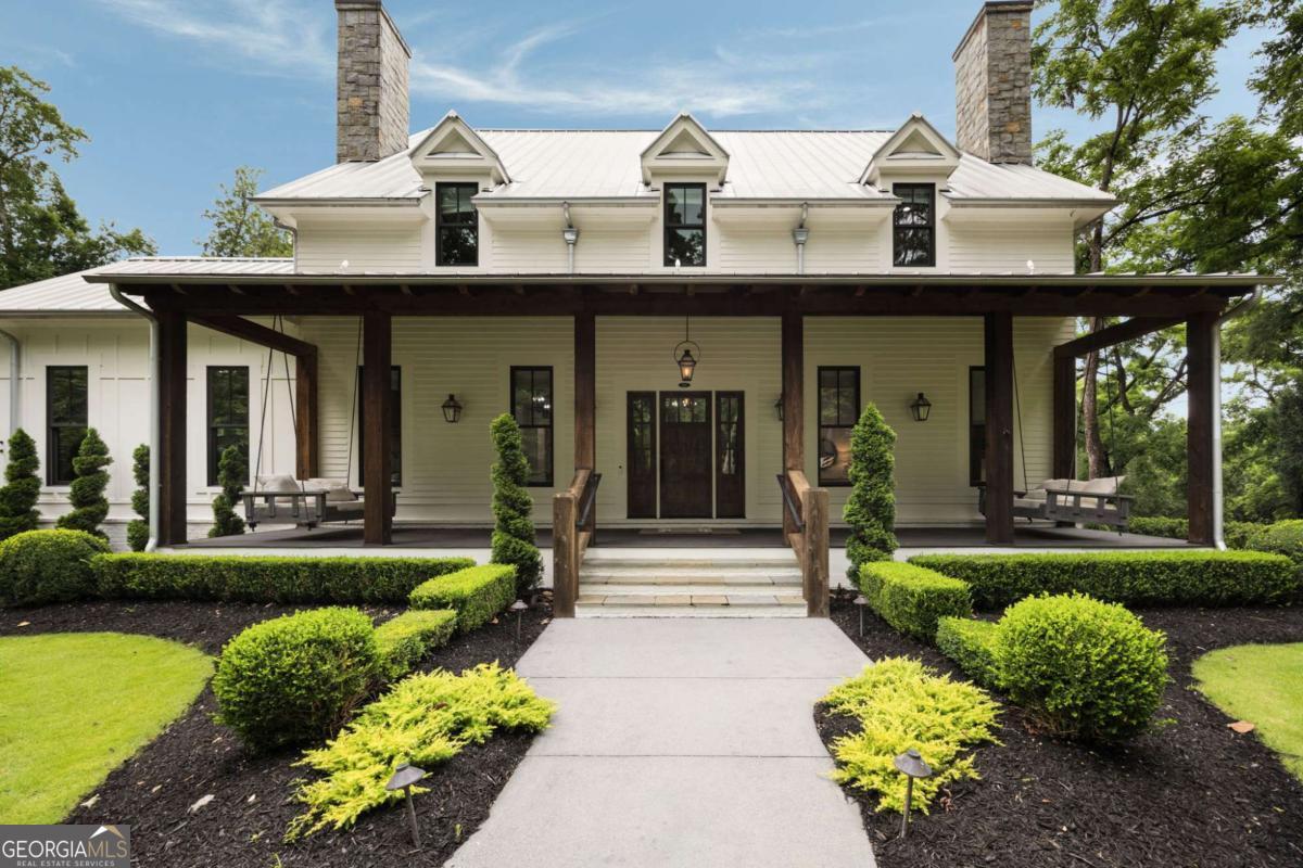 Welcome to your own private retreat in the heart of Milton. Set on 2.5 beautifully wooded acres behind a gated entry, this custom-built modern farmhouse by Steve Powell Homes combines timeless craftsmanship with the laid-back luxury of resort-style living. With a heated saltwater pool and spa, outdoor fireplace, and a backdrop of century-old oaks, this home offers the kind of privacy and setting that's getting harder to find. From the moment you step onto the front porch, framed by cedar beams, gas lanterns and tongue-and-groove ceilings, you'll feel the attention to detail that sets this home apart. Inside, 12-foot ceilings, reclaimed Pennsylvania barn wood floors, and natural light at every turn create a bright, welcoming feel. The fireside family room opens into a chef's kitchen with quartzite countertops, a high-end appliance package, large center island, and walk-in pantry. Accordion-style doors lead to a vaulted, wood-lined lanai-an all-seasons space with a fireplace that flows effortlessly into the pool and patio area. The main-level primary suite is a true escape, featuring a spa-like bath with heated floors, a soaking tub, dual showerheads, and a custom walk-in closet with a packing island. Just off the closet, the laundry room is a workhorse-with space for two washers and two dryers, tons of cabinetry, a work island, built-in desk, and drop zone. Whether you're managing a busy household or prepping for travel, this space makes life easier. Upstairs, you'll find four generously sized en suite bedrooms, each with custom walk-in closets, plus a versatile bonus room and a cozy reading nook that's perfect for quiet moments or homework hangouts. The finished terrace level adds even more to love-a full home theater, a flex space that works well as a gym or guest suite with its own full bath, and a fourth-car garage that easily doubles as a workshop or extra storage. Need more room to spread out? Above the main garage, an additional finished space offers endless potential-whether it's an in-law suite, a game room, or your go-to spot for entertaining. From the Control4 smart home system and full-house generator to the winding drive, professional landscaping, and extra parking pads, no detail has been overlooked. Zoned for top-ranked Cambridge High and just minutes to Downtown Alpharetta, Avalon, and GA-400, this property offers the rare mix of privacy, convenience, and laid-back luxury that's getting harder to find.