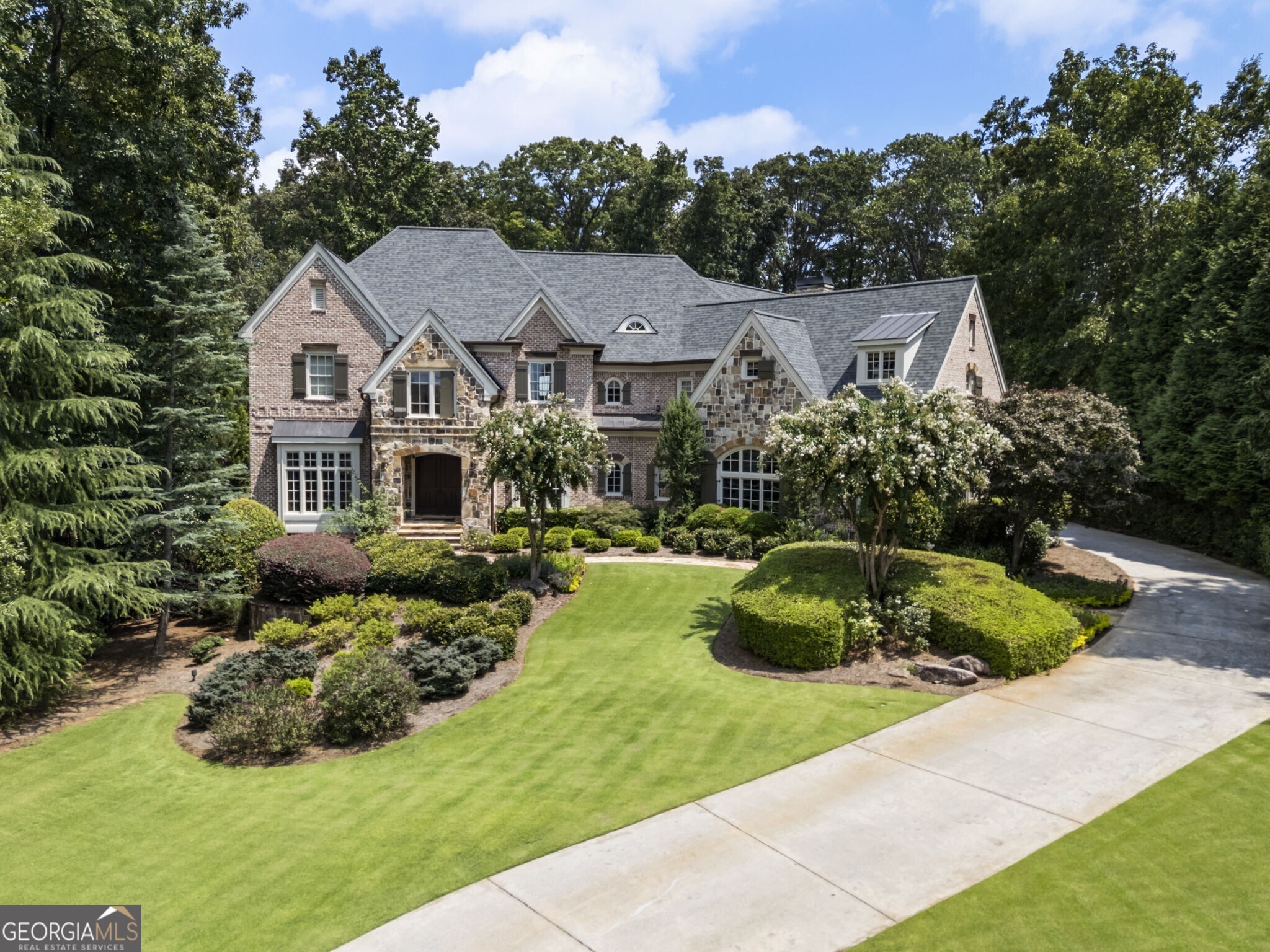 Welcome to this exquisite estate located in this sought after gated community in Milton where classic craftsmanship blends seamlessly with modern luxury. From the moment you arrive at the property, you are captured by the outside of the home and the custom stone and brick facade with all of the lush landscaping that sets the tone for a home designed to impress and built to endure. Step inside to a soaring foyer featuring a sweeping staircase and custom wrought iron railing that opens to the gorgeous dining room and main level. Multiple living areas offer warmth and versatility, showcasing coffered or beamed ceilings, architectural accents, stone fireplaces, and walls of windows that flood the rooms with natural light. Whether hosting guests or enjoying quiet evenings at home, these spaces embody comfort and sophistication. The gourmet kitchen overlooks the warm and welcoming keeping room with stone fireplace features rich custom cabinetry, professional-grade appliances, and expansive granite counters with double islands perfect for entertaining. This seamless blend of elegance and function is designed for culinary excellence and everyday living. Formal and casual dining spaces each provide their charm-from a chandelier-lit dining room with dramatic wood beams to a sunlit breakfast nook overlooking the gardens, outdoor decking, screened porch, covered patio and pool area. A richly paneled study with custom built-ins and a bay window creates a refined setting for work, reading, or reflection. A beautifully appointed main level guest bedroom and bath offers comfort and convenience, while two main level powder rooms feature designer finishes and modern fixtures, ensuring style and function. Upstairs, the primary suite is a true sanctuary including a spacious layout with a sitting area and fireplace, spa-inspired bath, and generous dual walk-in closets. Three secondary bedrooms include ample closet space and easy access to well-appointed baths, providing comfort for family and guests alike. A large recreation room anchors the upstairs, offering endless possibilities as a media lounge, playroom, or casual gathering space. Step outside to your private oasis. A sparkling pool with a cascading waterfall, lush landscaping, and an inviting fire pit and hot tub area provide the perfect backdrop for relaxation or entertaining. Multiple outdoor living areas, including a spacious deck and covered screened-in porch, make indoor-outdoor living effortless. The home's unfinished basement, with a generous footprint, presents an incredible opportunity to customize and create the ultimate extension of your living space while offering wonderful storage space. Throughout the home, thoughtful details-hardwood floors, designer lighting, and impeccable craftsmanship-add depth and character. Every corner of this residence reflects timeless design and modern ease. The gated community ensures privacy, security, and a true sense of retreat, while being just minutes from top-rated schools, shopping, dining, and the heart of Milton. This is more than a home; it's a lifestyle. Don't miss the opportunity to own one of Milton's most exceptional properties in The Manor.