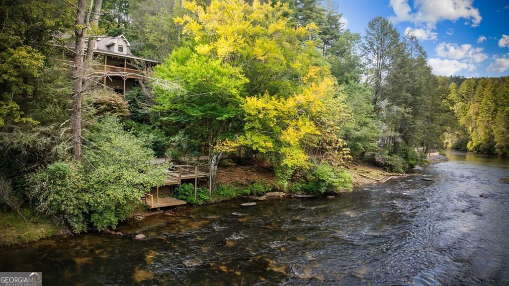 Fronting one of the widest and most beautiful stretches of the Toccoa River, this extraordinary home epitomizes luxury and comfort in a truly unmatched riverfront setting. Nestled in the heart of the Aska Adventure Area, you'll enjoy close proximity to miles of hiking and biking trails as well as the surrounding National Forest. The open main level features warm wood floors, a striking stone fireplace with gas logs, and walls of glass that frame sweeping river views while seamlessly blending indoor and outdoor living. A chef's kitchen with granite countertops, stainless appliances, a gas range, and a large center island flows effortlessly into the spacious dining area, creating the perfect space for gatherings. The primary suite is a private retreat with access to both a screened porch and a riverfront deck, along with a spa-like bath offering double vanities, a soaking tub, tile shower, and an oversized walk-in closet. A convenient laundry closet is also located on the main level. Upstairs you'll find two vaulted bedrooms, a full bath, and a versatile loft-style living area with additional sleeping space. The finished terrace level expands the living area with a second stone fireplace, full wet bar, pool table, bedroom, and full bath. The lower deck includes a hot tub and easy steps leading down to the river-perfect for fishing, kayaking, or simply floating the day away. Outdoor living is exceptional, with a huge covered porch overlooking the river, a fire pit, and a rare private fishing dock directly on the water. With unspoiled Toccoa River frontage, easy access to the water, and offered fully furnished and turn-key, this property delivers a lifestyle that is both remarkable and nearly impossible to duplicate.