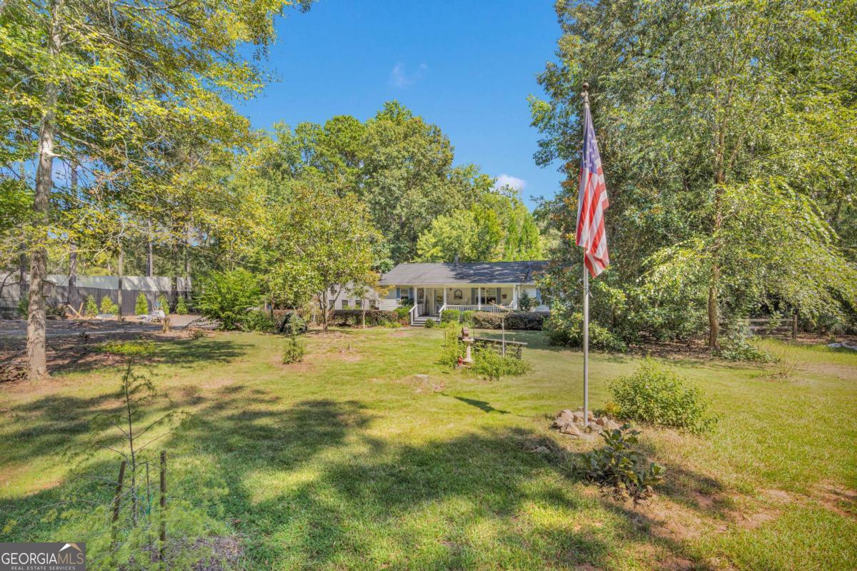 Rare opportunity to own a charming 3-bedroom 2-bathroom ranch on 3.44 acres in highly desired Morgan County! Located on a short quiet gravel road in Buckhead, this rustic retreat welcomes you with a gated driveway and peace that only quietness can provide. As you walk through the front door the vaulted ceilings and pine flooring make the open floor plan feel bright, spacious, and inviting. A wood-burning stove, and a cheerful country kitchen with the perfect pop of color and stonework adds character and warmth. Step outside to a large covered back deck-perfect for early morning coffee, host family gatherings, overlooking the mature garden, or simply enjoying the wildlife. The property also features a two-car detached garage with workshop space and two additional storage rooms. The rocking chair front porch, multiple shaded sitting areas within the garden, and a fully fenced yard add to the appeal. There is a dog kennel on the property, and the property line extends past the fence into the woods to a dry riverbed where deer travel in the evening. Lovingly cared for by the same owners for nearly 20 years, this home has true character and is a peaceful and private retreat just minutes from Lake Oconee and historic Madison. Property owner realizes the home needs additional TLC and is priced accordingly. Property sold as is.