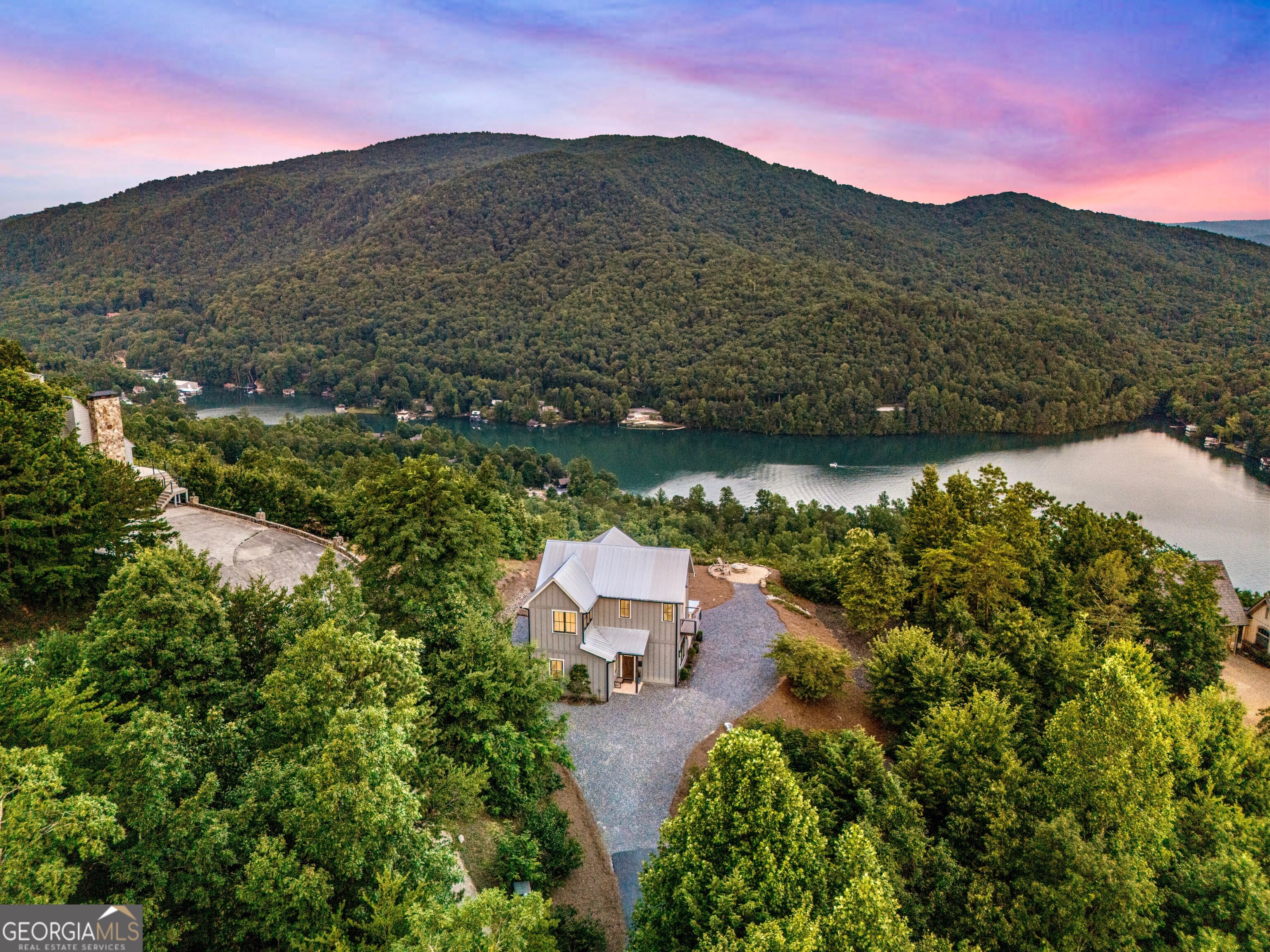 Located in exclusive Goat Cliff Estates, this 3-Bedroom + Loft, 2-Bathroom home offers a rare opportunity to own a piece of North Georgia paradise (fee-simple) with deeded lake access and dock house. This home has one of the best views of all of Lake Burton. Designed to embrace the outdoors, this elegant mountain retreat boasts sweeping layered mountain vistas and spectacular sunrise and sunset views overlooking Lake Burton. Step inside to an open-concept living area with high ceilings (10, 14+ throughout), large picture windows, and warm wood accents that create a sense of comfort and grandeur. The well-appointed kitchen opens seamlessly to the living and dining spaces, perfect for entertaining guests with a large seven-foot island and custom-built cabinetry. The spacious primary suite offers a private sanctuary with stunning views, a spa-like bathroom including a large overhead rain shower, and soaking tub with sunset views. Two guest bedrooms on the main level provide ample room for family or visitors. Outside, enjoy a porch that's ideal for morning coffee with incredible long mountain views or enjoy sunset cocktails while sitting around the masonry outdoor fire pit overlooking the lake. As part of the Goat Cliff Estates community, residents enjoy shared deeded lake access and a dock house, allowing for boating, kayaking, and lakeside recreation. With its unmatched views, and convenient location only minutes from Waterfall Club, Anchorage Boat Dock and the amenities of Downtown Clayton, 714 Sonya Road is a rare gem in the Lake Burton market (on the preferred north end of the Lake) whether you're seeking a luxurious full-time residence or a weekend escape.
