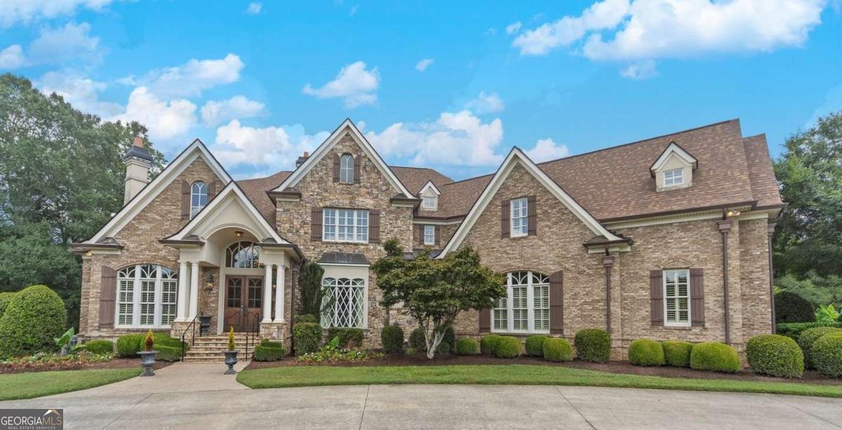 Welcome to this stunning four-sided brick executive estate situated on 7+ private acres featuring a spring-fed, 2-acre stocked pond. This luxurious residence offers elegant architectural details, custom trim throughout, and soaring ceilings designed for both grand entertaining and comfortable everyday living. The two-story foyer with a curved staircase and iron balusters sets the tone for the home's craftsmanship. French doors lead to a vaulted library with exposed beams, marble gas fireplace, and built-in bookcases. The main-level owner's retreat features a sitting area with fireplace, private coffee bar with sink and refrigerator, custom walk-in closet, and a spa-inspired bath with dual shower heads, whirlpool tub, double vanities, and a picture window overlooking the pond. The heart of the home is the chef's kitchen, complete with: Wolf 6-burner + griddle & double oven, Sub-Zero refrigerator & stainless appliances including Wine cooler, ice maker, warming drawer & butler's pantry. Angled butcher block island & breakfast room with wall of windows Enjoy multiple living spaces including a two-story great room with coffered ceiling, gas fireplace, built-ins, and a wall of windows plus family room off the kitchen with 2 walls of windows, fireplace and bookcases. Formal banquet-sized dining room with columns and heavy trim detail. Biltmore Style back patio with stamped concrete & curved stairs to private backyard The upper level offers 4 generously sized bedrooms and 3 full baths. The finished terrace level is an entertainer's dream, featuring a great room, rec room, theater room, bar with dishwasher & sink, wine cellar, bedroom, full bath, and access to the covered stamped-concrete patio overlooking the pond. Additional features include: 3-car side-entry garage, laundry room with sink & cabinetry, central vacuum system, whole-house generator, irrigated by designated private well and new roof, circular driveway with ample parking ideal for entertaining. Convenient to shopping, medical, airport & Battery (home of the Braves) Experience the perfect blend of privacy, luxury, and serene outdoor living in this breathtaking estate.