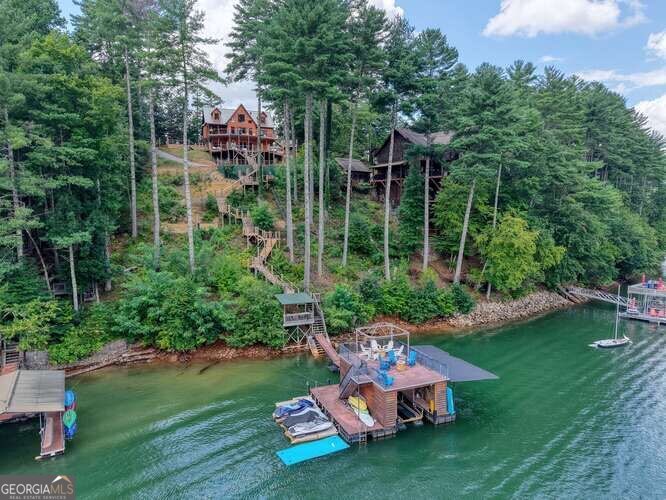 Discover your deep-water sanctuary in this inviting Blue Ridge lake home, perfectly situated within the highly sought-after gated community of Browns Cove in the heart of the picturesque Aska area. This cabin offers a rare blend of rustic charm and spacious living, with breathtaking lake and mountain views that can be enjoyed from nearly every room. Whether you're seeking a peaceful full-time residence, a seasonal retreat, or a vibrant vacation getaway, this property provides an incredible canvas to create your dream lakeside lifestyle. Step inside the main floor and be welcomed by a large master suite designed for comfort and privacy. The expansive living room, featuring a dramatic floor-to-ceiling stone fireplace, invites cozy gatherings and memorable evenings with family and friends. Adjacent to this, an oversized dining area overlooks the kitchen, creating a warm and open atmosphere perfect for entertaining or enjoying quiet meals while taking in the stunning views. Venture upstairs to find two generously sized bedrooms connected by an open walkway, along with a full bathroom - offering plenty of space for guests or family members. The basement level is a true highlight, boasting an exceptional entertainment area complete with a built-in bar, a comfortable guest bedroom with a full bath, plus an additional bunk room with a game nook - ideal for kids or visitors to unwind and enjoy their own space. The home's multi-level decks extend your living area outdoors, providing serene spots to relax, entertain, or simply soak up the spectacular scenery. For effortless lake access, a private tram transports you directly down to the deep, beautiful waters of Browns Cove, making swimming, boating, and fishing a breeze. This cabin presents a fantastic opportunity to personalize your mountain lake retreat with modern touches or maintain its cabin-like warmth. Call today to view!