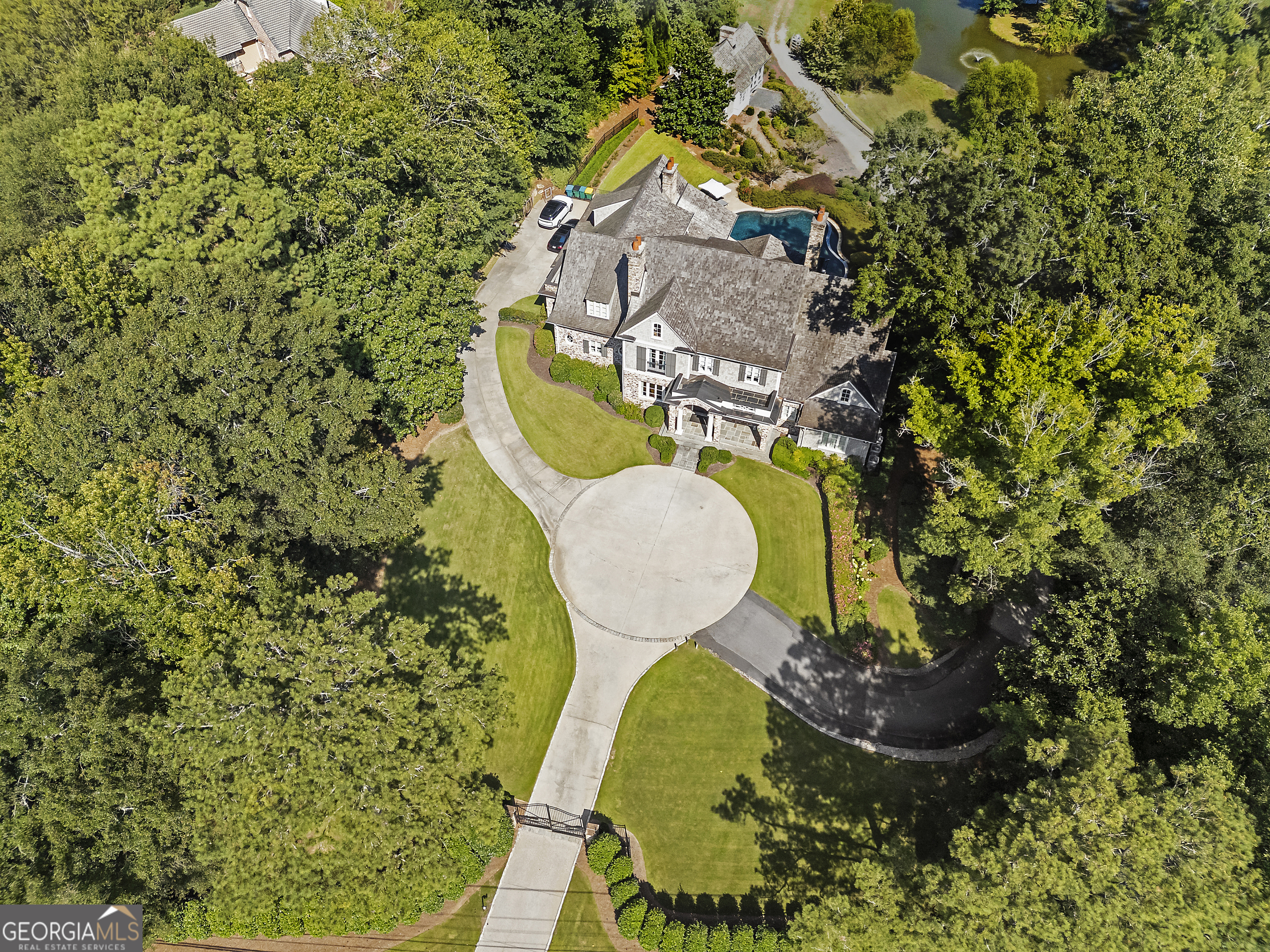 Tucked away in a serene and private setting, this extraordinary Buckhead gated estate spans 6.8 acres of manicured gardens, lush lawns, and wooded privacy - offering the rare opportunity to enjoy both refined living and natural beauty in one remarkable retreat. From the long, picturesque drive to the grandiose stone fa ade, every detail sets the tone for timeless elegance. The main residence blends architectural charm with modern amenities, featuring expansive windows, multiple outdoor living spaces, and a resort-style pool with an integrated spa as the centerpiece of the grounds. Upon entering the home, you're greeted by a light-filled foyer that opens to the formal fireside living room, adorned with custom bookcases, double doors that lead to a private balcony overlooking the pool, and sweeping property. At the heart of the home, the chef's kitchen is both functional and sophisticated - complete with Wolf and SubZero appliances, double Bosch dishwashers, a breakfast nook, a wet bar with refrigeration, and a generous pantry. The fireside keeping room off the kitchen creates a multi-use space perfect for busy mornings and afternoons. The main level also boasts a formal dining room, office, laundry room, and mudroom. The luxurious primary suite, designed as its own perfect oasis with a fireplace, dual custom closets, and a spa-like bath with soaking tub, separate shower, and dual vanities, is the perfect everyday retreat. Upstairs, you will find a long hall perfect for displaying photos and art that leads to the four guest suites, each boasting its own ensuite bath. The loft space is perfect for an additional office or hangout space. Additionally, there is a charming bunk room that offers plenty of room for relaxation, play, or hosting friends and family. The terrace level is dedicated to leisure and entertainment, offering a fireside living room and a full kitchen. The temperature-controlled wine cellar is a dream, adorned with a black steel and glass door. This is a wine connoisseur's dream. The game room, billiards space, and home theatre create a fun atmosphere on the terrace level. Adding to the amenities of this home, a home gym and full bath are located on this level. The property includes a charming guest house that feels like a private mountain retreat. With its cottage-inspired design, it offers a fireside living area, kitchenette, loft bedroom, private bath, and a screened porch overlooking the serene pond-ideal for visitors or a creative sanctuary. Beyond the homes and gardens, the estate reveals a collection of rare lifestyle amenities that set it apart. At its heart lies a private, full-sized baseball field-a truly extraordinary feature that transforms afternoons into cherished memories. Whether it's perfecting your swing during a quiet round of batting practice or hosting an impromptu weekend game with family and friends, this one-of-a-kind addition brings a sense of play and possibility to the property. Every detail of this estate has been curated to deliver a lifestyle that feels both elevated and effortless. With its seamless blend of luxury, comfort, and privacy, it offers the ambiance of a private resort. For those who value timeless elegance paired with modern convenience, this residence is more than a home; it is a sanctuary, an experience, and a legacy to be treasured.
