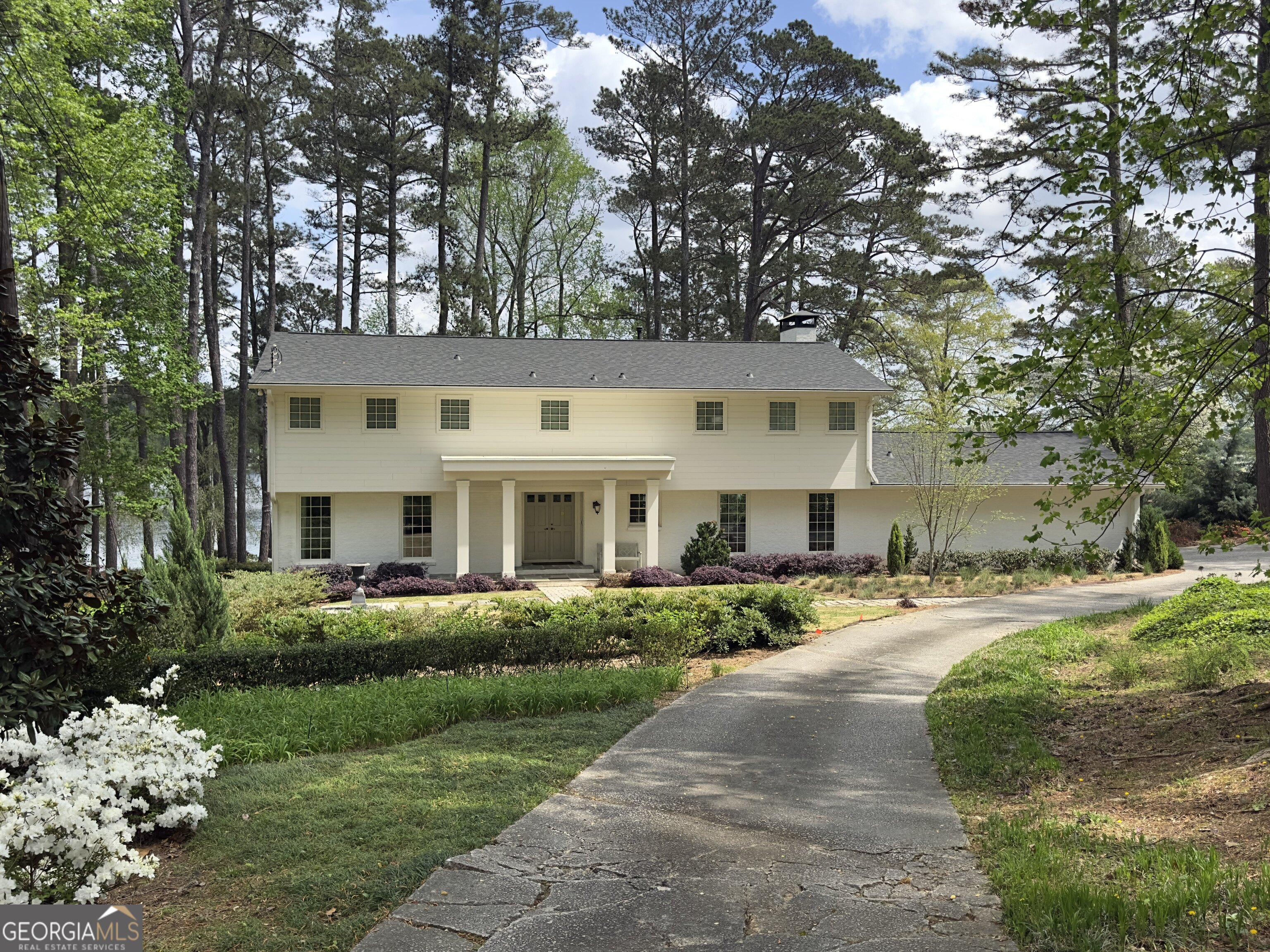 This house is a treasure. An exquisite two-acre, deep-water, terraced lakefront lot on private Lake Spivey. Over 214 feet of pristine lakefront, perfect for all activities like fishing, skiing, sailing, and rowing. The highlight of the lot is the magnificent stone seawall with a spacious brick patio projecting into the lake, complemented by a charming, Greek Revival-inspired, award-winning boat dock. The shoreline infrastructure provides an ideal setting for large gatherings of family and friends, offering incomparable views of the lake and the spectacular fireworks display on the 4th of July. The house has a northeast exposure on the lakeside, which allows for stunning sunrises over coffee and moonrises over cocktails from either the second-story deck off the primary bedroom or the first-floor deck and terrace. Both locations are perfect for taking in focused views of the lake over a garden where something is in bloom every season. The seamless transition from indoors to outdoors makes the house, shoreline patio, and dock ideal for every gathering. The architecture is traditional, with a welcoming porch leading into 3200 square feet of light-filled charm, including five bedrooms and four bathrooms. Beautiful hardwoods on the first and second floors. One guest bedroom and the primary bedroom both have en-suites. The primary bedroom boasts a cozy sitting area and a contemporary fireplace that can be enjoyed from either the bed or the sitting area. The open floor plan of the kitchen flows into a spacious and warm family room enhanced with rare wormy chestnut paneling, accentuated by an oversized fireplace. Both the family room and dining room area overlook the lake with a wide wall of windows showcasing the gently sloping terraced garden. The full bath on the first level accommodates swimmers and boaters and their gear. Downstairs offers an additional 1300 square feet of buildable space. Experience all the peace and tranquility of lake living, just 5 minutes from I-75, 20 minutes from Atlanta International Airport, 25 minutes from downtown Atlanta, and 30 minutes from Atlanta's premier shopping districts. Costco and Starbucks are a mere 7 minutes away, along with a variety of restaurants and other conveniences. Altogether, this property has an overwhelming sense of place - it's pure magic!