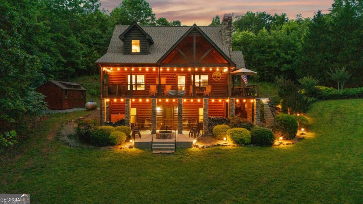 Set against a backdrop of seasonal mountain views and lush landscaping, this stunning cabin in Brown Haven Heights offers the charm of mountain living with the comfort and flexibility of a thoughtfully designed home. Inside, cathedral ceilings and floor-to-ceiling stacked stone fireplace creates a warm welcome, while the open-concept layout flows effortlessly through the spacious living area, dining space, and kitchen-complete with stainless steel appliances and a unique hand-crafted stair railing for a personal touch. The main level features a large bedroom with tongue-and-groove ceilings, full bath, and laundry room. Upstairs, a loft opens to a private owner's suite with a walk-in closet, tiled shower, and jetted soaking tub. The terrace level offers even more room to unwind or host, with a second living area, game room, partial kitchenette, full bath, and oversized bedroom-ideal for guests or multi-generational living. Outside, a wraparound porch leads to a patio and fire pit area - especially loved for peaceful evenings under the stars. A detached workshop, tankless water heater, and paved access add to the ease of ownership. Whether you're seeking a full-time residence, mountain escape, or investment, this cabin is a perfect match-just minutes to Lake Chatuge, dining, shopping, and the best of Hiawassee.