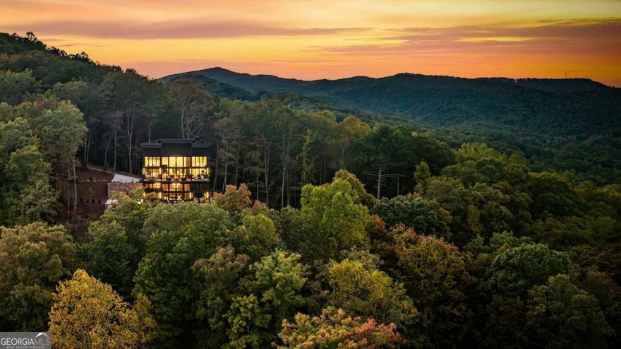 Welcome to 321 Skylight Drive, a rare luxury retreat in the coveted Aska Adventure Area only a short stroll to the Toccoa River and moments from renowned hiking and biking trails and Lake Blue Ridge. Tucked away on a private mountain-view lot with layered long-range vistas and all-paved access, this home blends upscale design with a timeless mountain setting. Step inside and be greeted by soaring cathedral ceilings, walls of glass, and a striking fireplace anchoring the open-concept living space. The gourmet kitchen is designed for entertaining, with commercial-grade appliances, custom cabinetry, and a spacious island that flows seamlessly into a generous dining area. Glass sliders lead to an expansive covered deck, complete with a stone fire table and panoramic views perfect for four-season outdoor living. With five ensuite bedrooms plus a bunk room, every guest enjoys privacy and comfort. The bathrooms are truly spa-like, featuring designer tile, statement lighting, large showers, and in the primary suite, a soaking tub, dual vanities, and a custom walk-in closet with an in-closet laundry station. The terrace level is built for relaxation and entertainment, showcasing a spacious den with fireplace, billiards area, wet bar, and glass doors opening to a stone patio with a heated jacuzzi pool. Every detail in this residence reflects glamorous mountain-rustic luxury, where warm natural textures meet modern sophistication. Sold fully furnished, this exceptional property offers a turn-key investment or private mountain sanctuary in one of North Georgia's most desirable locations.