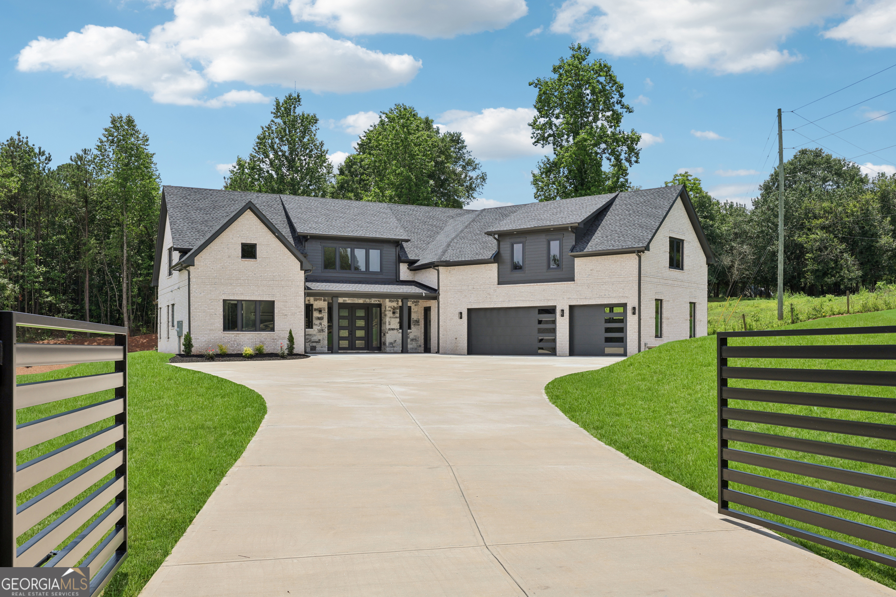 Welcome to this custom-built modern estate offering 5,053 square feet of luxury living on 1.19 private acres in Braselton, GA. With no HOA and a gated driveway, this 4-bedroom, 4.5-bath home blends modern design, smart home technology, and exceptional privacy. Inside, you'll find soaring ceilings, wide-plank hardwood flooring, and oversized European windows that flood the home with natural light while delivering superior efficiency. Foam insulation has been installed throughout the home, providing enhanced comfort and energy savings year-round. The open-concept living area features a custom fireplace with floating wood shelves and a modern tray ceiling with LED accent lighting. The home is equipped with smart home features throughout, offering enhanced convenience, comfort, and security. The chef's kitchen includes an oversized waterfall quartz island, custom two-tone cabinetry, premium gas cooktop, double ovens, full-height designer backsplash, and a hidden walk-in pantry. The spacious primary suite features vaulted ceilings with wood accents, a feature wall, and a spa-like bath with an oversized walk-in shower, freestanding soaking tub, dual vanities, and designer tilework. Additional highlights include a large mudroom with custom built-ins, a well-equipped laundry room with extra cabinetry, a spacious bonus room with wet bar and built-in shelving, and multiple flex spaces for work, entertainment, or fitness. The oversized 3-car garage features modern glass-panel doors, while the expansive concrete driveway allows ample parking. The septic system is located on the side of the property, leaving plenty of room in the backyard to add a pool or outdoor living space. A gated entrance provides privacy, and the property enjoys peaceful views of a neighboring property with horses, all while remaining conveniently close to Braselton's shopping, dining, and commuter routes. This modern estate offers a perfect balance of privacy, freedom, technology, and sophisticated design.