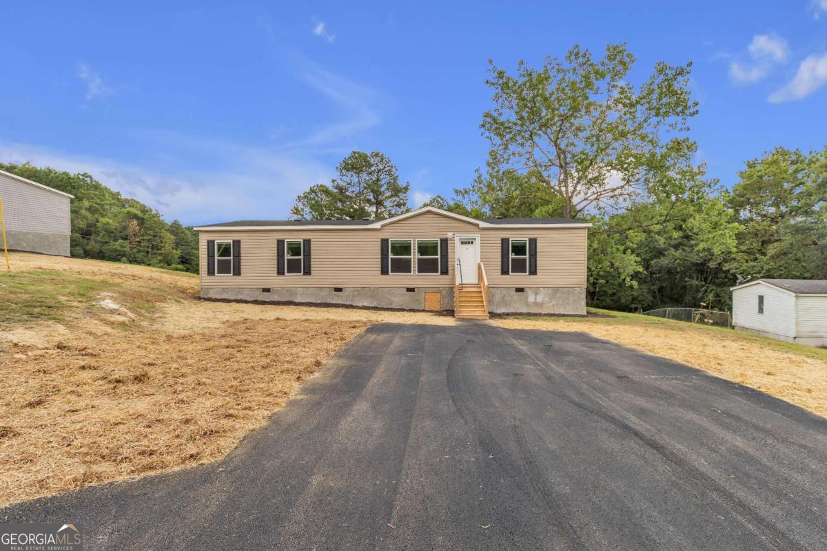 Move-In Ready Double Wide on Spacious Lot! Within 2 miles of Lake Allatoona! Welcome home to this brand new, never-lived-in double wide manufactured home situated on a generous lot in a peaceful rural setting. Featuring an inviting front porch and a rear entry with new wood decking, this home offers both curb appeal and functionality. Inside, you'll find a bright, open floor plan with stylish, low-maintenance LVP flooring throughout the main living areas. The spacious living room flows seamlessly into a modern kitchen complete with an oversized island, abundant cabinet space, durable countertops, and black appliances including stove, refrigerator, and dishwasher. Adjacent to the kitchen is a designated dining area with large windows for natural light. The split-bedroom layout provides privacy with a large primary suite featuring a walk-in closet and large private bath. The en suite bath includes a spacious vanity, tub/shower combo, and modern finishes. Two additional bedrooms (both with walk-in closets) share a second full bathroom, perfect for guests or family. A dedicated laundry/mudroom with exterior access adds convenience and functionality. Outside, enjoy a large, open lot with plenty of room for a garden, play area, or future outbuildings. Paved parking and fresh grass and mulch give this property a clean, finished look. HVAC is also brand new! If you're searching for affordable, move-in ready living in a serene location, this home is ready to welcome you.
