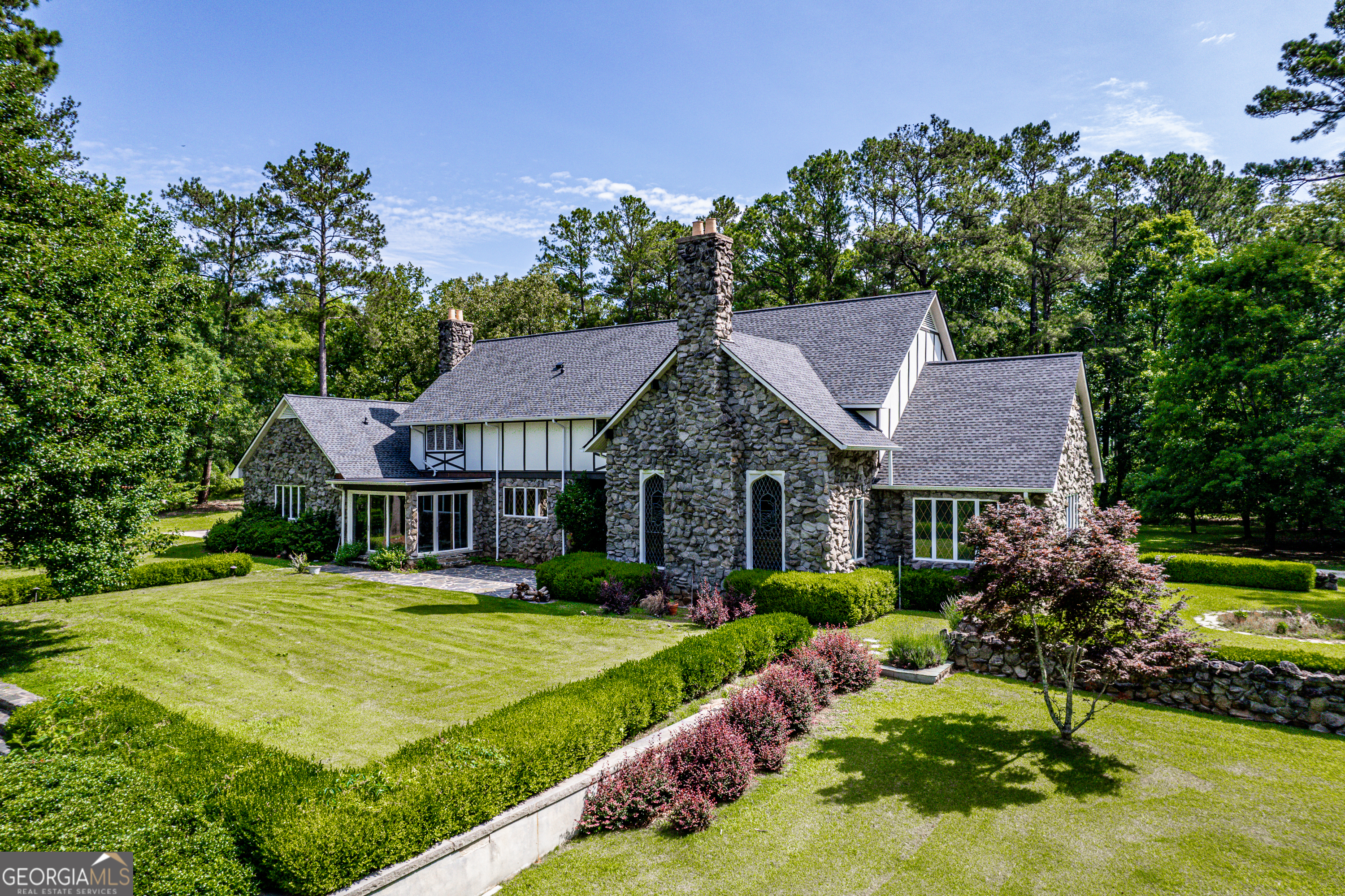 Step into a world where timeless elegance and old-world charm meet modern comfort. Greystone is a breathtaking 5,500 square foot Tudor-style manor set amid 73 acres of pristine, rolling countryside. A rare fusion of architectural grandeur and natural beauty, this extraordinary estate is perfectly suited for refined living, outdoor recreation, and legacy ownership. As you pass through the gates, a sense of serenity and seclusion welcomes you. Manicured trails weave through wooded groves and fenced pastures, ideal for peaceful walks, trail rides, or ATV exploration. At the heart of the property lies a stunning four-acre, spring-fed pond fully stocked and framed by vibrant foliage. This serene waterscape offers year-round enjoyment, from casting a fishing line to watching the seasons reflect in the still waters. Greystone is thoughtfully equipped for equestrian and outdoor lifestyles, featuring a two-stall horse barn, fenced paddock, and a private outdoor range suited for pistol, rifle, and archery use. The land is rich with wildlife including deer and wild turkeys, providing excellent opportunities for hunting or observing nature in its purest form. The manor home itself is a showcase of craftsmanship and design, constructed with lasting materials including grey feather rock and rare imported English stone. The castle-like facade recently enhanced with a brand-new roof, evokes storybook charm and stands as a testament to enduring quality. Inside, the homes sophistication is immediately apparent. Rich walnut-paneled walls lend an air of tradition rarely seen in modern construction. Gleaming parquet floors stretch across grand spaces, while a magnificent U-shaped staircase unites the lower level with the upper bedroom wing. Thoughtful architectural details such as antique fixtures, intricate woodwork, and leaded-glass doors are found throughout. The great room, with its soaring cathedral ceilings, massive wood-burning fireplace, and two oversized stained-glass windows, creates a breathtaking centerpiece for gathering and entertaining. Adjacent is a cozy family room with a gas-burning fireplace, which opens to a light-filled sunroom perfect for relaxing through every season. French doors lead to an expansive slate patio and grassy terrace, where you can dine alfresco, entertain guests, or simply take in the panoramic views of the pond, gardens, and surrounding woodlands. From every window and outdoor space, nature provides a spectacular backdrop. The luxurious owners suite offers a private retreat with its own fireplace and elegant finishes. Additional bedrooms are spacious and comfortable, ideal for family and guests. A separate two-bedroom, two-bath guest house connected to the main residence via a grand porte-coch re mirrors the Tudor style and stonework, offering independent living space for visitors, extended family, or caretakers. Though steeped in history and countryside charm, Greystone offers the conveniences of modern living. High-speed internet (100 Mbps) makes remote work and streaming seamless, ensuring the estate is as functional as it is picturesque. Located just five minutes from Interstate 20, Greystone provides easy access to regional destinations. Lake Oconees recreational offerings and medical facilities are just 30 minutes away, while the cultural hubs of Augusta, Athens, and Atlanta are within an hours drive. Whether youre seeking relaxation or connection, this estate offers the best of both worlds. Greystone is more than a home it is a sanctuary, a storybook escape, and a place to build a legacy. Whether you envision it as a full-time residence, a seasonal retreat, or a generational estate, Greystone stands ready to fulfill your vision with unmatched beauty, character, and grace.