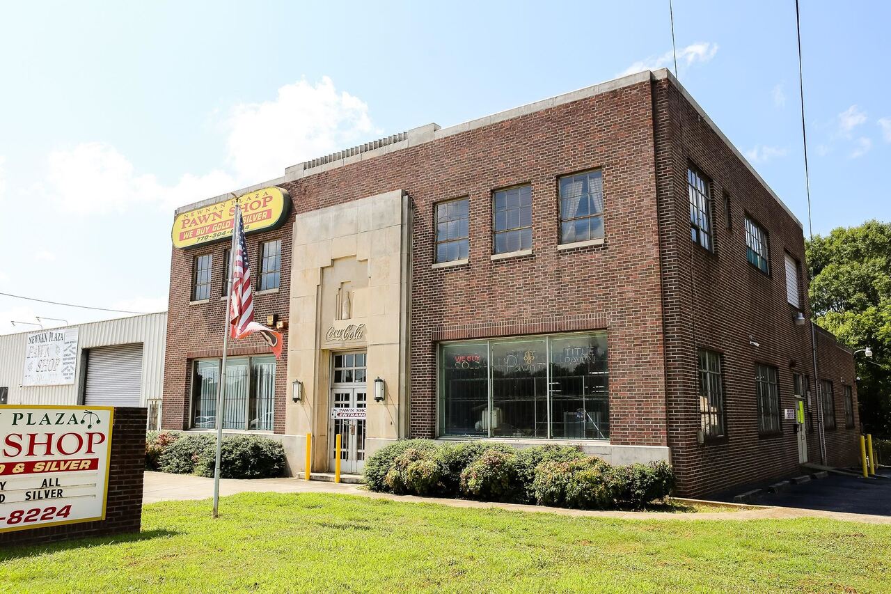 Take a step back in time and have the opportunity to own one of the original Coca-Cola bottling buildings.  Estimate build date shows 1935 but some records show 1905.  What a fabulous location this building is and a great investment.  The buildings sit on 1.3 acres. The original building is built of all brick and steel.  It has right at 5000 square feet of space on the main floor that includes a wide open room with tons of possibilities, storage room, 2 private offices with a 1/2 bath.  The original entry way of the building is still there.  The upstairs features a 2850 square foot finished apartment with all hardwood flooring, kitchen, bar, living areas, private bedroom, walk-in closet and laundry room.  The views from the apartment are amazing!  There is a dumbwaiter that goes from the warehouse to the upstairs apartment.  The warehouse was added in the 1960's  and the current grocery store/warehouse space is~8700 square feet. There is a loading dock, paved parking in the front, sides, and rear.  The rear of the property is completely fenced in.  The basement is 3135 square feet, has a concrete floor, what could be a re-finished bathroom, storage room, and the original boiler and parts are still there.  There is also a 6 bay 4350 square foot garage that was the original bottling truck warehouse and bottle warehouse, some of the interior walls are the original wood with original wood ceilings, the floor is concrete and full exterior brick.  And there is an additional 2 bay garage on the side of the building.  This location is perfect!  walking distance to downtown Newnan and minutes to I-85!  Please call to make an appointment to see or show, must be shown by appointment only.