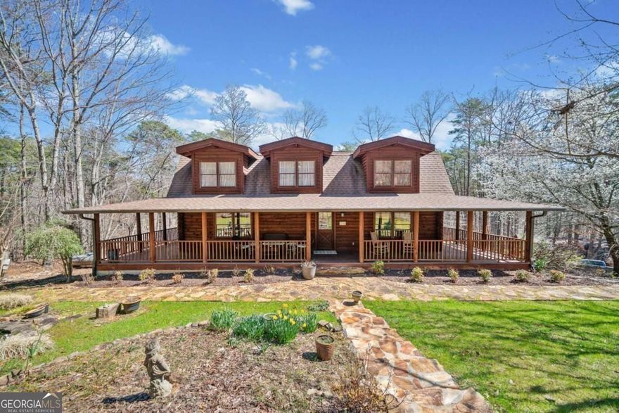 Cape Cod-style log home tucked away on 12.54 acres. It is built with high-quality materials and features rich heart pine wood floors, vaulted beamed ceilings, and a welcoming wraparound porch on all four sides. The kitchen has granite countertops, a white farmhouse sink, a spacious island, and a cozy second fireplace. The two-story great room features a brick fireplace, vaulted ceilings and exposed beams. The main-level primary suite provides convenience with an attached bath, which has been recently updated to include a handicap-accessible shower. The upper level has three additional bedrooms, each of which shares a hallway bathroom. Downstairs, the unfinished basement includes of a full bath with the potential for extra living space. Outside, a separate screened-in party pavilion is perfect for gatherings, while the barn workshop, complete with second-floor storage and an additional equipment outbuilding, provides ample space for hobbies and storage. A professionally installed whole-house generator ensures peace of mind. Lush landscaping, blooming perennials, and a small creek running through the property add to the charm of this one-of-a-kind escape.
