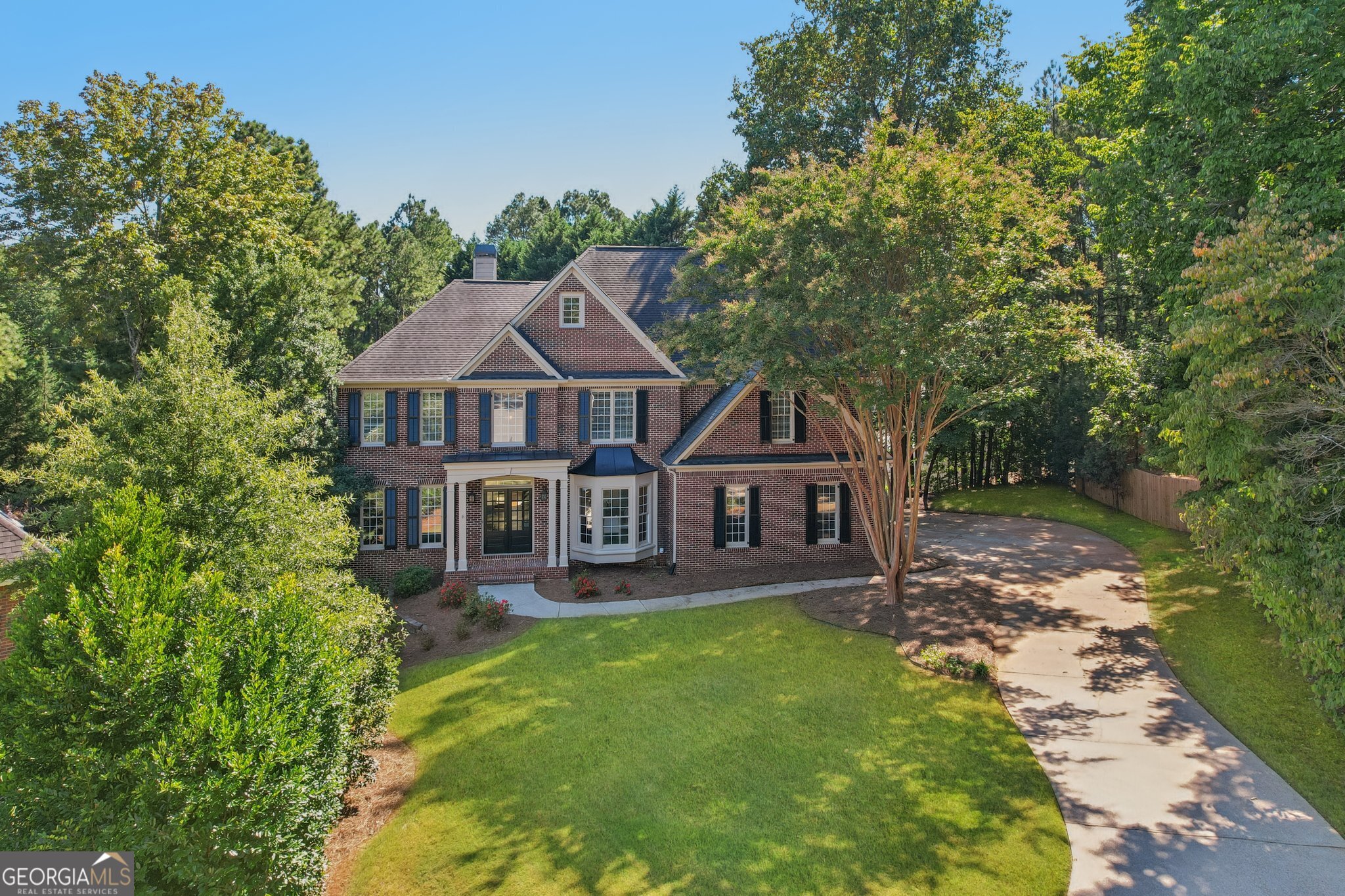 Welcome to this stately brick residence that blends timeless curb appeal with modern comfort. From the moment you arrive, the long driveway, lush landscaping, and classic front porch set the tone for a home designed for both elegance and ease. Inside, the soaring 2-story great room with its dramatic stone fireplace and wall of windows creates a stunning focal point, while the open layout flows seamlessly into the kitchen and breakfast area. With granite counters, stainless steel appliances, a center island, and abundant natural light, the kitchen is perfect for everyday living or entertaining. The spacious primary suite is a serene retreat, featuring a sitting area surrounded by bay windows and a spa-like bathroom with dual vanities, soaking tub, and glass shower. Step outside to enjoy a private wooded backdrop from the covered deck or patio, ideal for relaxing afternoons. With thoughtful details throughout, generous living space, and a location in a desirable community complete with a playground, pool, racquetball, sidewalks, and tennis courts.