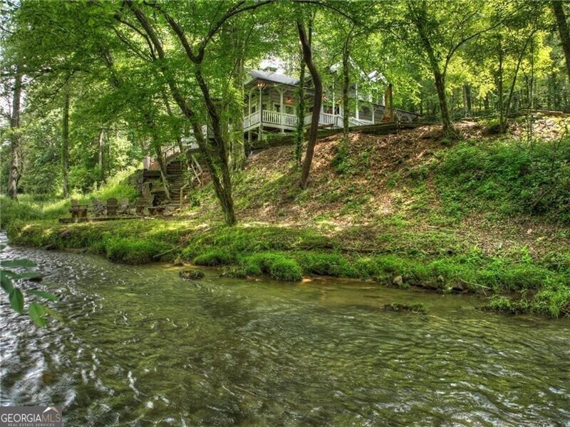 Exuding charm with its storybook setting, this handcrafted, true dovetail log home in the heart of the North Georgia Mountains is truly one of its kind. Overlooking the rushing waters of Mountaintown Creek, rolling pastures, and a long range mountain view, this rustic retreat is an enclave destination that feels completely secluded all while conveniently located to Downtown Ellijay, Pinhoti hiking and biking trails, and numerous outdoor activities. Complete with three bedrooms, a large sleeping loft, sprawling living room with a masonry double-sided stone fireplace, soaring cathedral ceilings, and a warm wooden interior. The gourmet kitchen boasts an eat-in island, storybook dinette overlooking the creek, and a formal dining area. Off the kitchen guests will also find a sitting area next to the fireplace. The primary suite has its own fireplace for cozy nights in. The outdoor living spaces complete this whimsical lodge with wraparound decks, views across the horizon, and a creekside fire pit for nights under the stars. Find trophy trout and abundant wildlife in your own backyard at this gorgeous retreat. Call today for an exclusive tour!