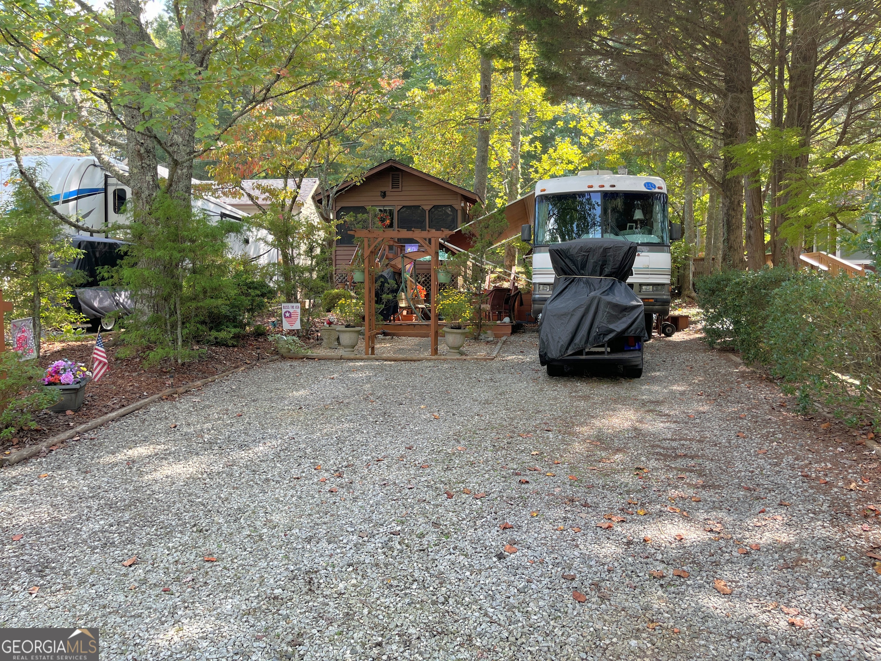 Come walk through an arbor on a stone walkway to a charming cabin nestled among shade trees, cedar trees, azaleas and multiple perennials. Inside the cabin there is a warm feeling from the Ponderosa pine walls and vaulted ceiling. It has custom Roman shades and is fully furnished with a sleeper sofa, table, chairs and an antique style electric heater. The Kitchenette has solid surface counters, solid wood cabinetry, pantry, a countertop oven and a newer full-size refrigerator. The roomy bath has a shower and three closets for your clothes and more storage. The water heater gives you almost instant hot water for your shower and Kitchen sink too! It has a small loft for napping, or storage as well! Outside you'll find a 12X24 deck with rope lights for evening ambiance and is perfect for relaxing in the swing or entertaining. There is another 8X8 deck with benches and a fire pit. The 1996 Holiday Rambler Endeavor has a queen bed and can serve for extra sleeping area with another sleeper sofa and bench/table that also converts to a bed. So, bring the family, grands, or friends to stay! There is a full Kitchen with oven/range, microwave, refrigerator and toaster oven. It has 2 TV's and a VHS player that could be fun! It's also equipped with a generator and has generous parking for 4 vehicles! You'll create a lifetime of memories here, whether you're relaxing, fishing, or participating in the ongoing activities within Paradise, a gated community. Enjoy the pool, pavilion, clubhouse, and planned activities! The location is central to all the fun in nearby mountain towns and events, just minutes from Cleveland, Helen, Dahlonega, Clarkesville, and Blairsville. Shop, dine, fish, hike, and visit vineyards-the possibilities are endless! Please note that Paradise is a vacation resort community that does not allow full-time living. The listing agents are owners in Paradise, so feel free to call for a tour or more detailed information about Paradise and this property.