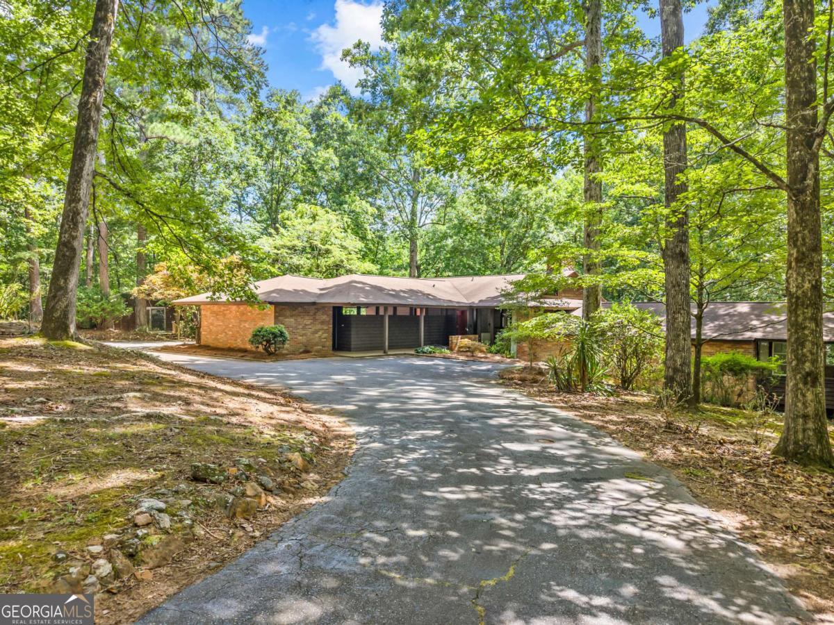 Designed by Frank Lloyd Wright Taliesin Apprentice and UGA professor Harold G. Wescott, this sprawling split level sits in harmony with the natural wooded 2.29 acre property surrounding it. This home was originally commissioned in 1964 by the late Earl and Mary McCutchen-local potters and art glass makers-who appreciated the Prairie style architecture that is so iconic of the period, which heavily influenced the mid-century modern designs. Upon entry you'll find vaulted ceilings with two-story fieldstone double fireplace made from stones sourced on the property during construction. The entry level fireplace is gas logs while the lower, den-level fireplace is woodburning. Additional features include 3 large bedrooms each with their own bathrooms (3 bathrooms) and a half bath as well as gorgeous updated kitchen with striking, earthy granite and loads of storage. The primary bedroom has nearly 270 degrees of open windows and also offers ensuite bath with a large vanity and six-yes six-closets. The living and dining areas open up onto a large patio overlooking the lovely property. Surrounded by windows, almost every nook of this home feels one with nature. The den and third bedroom open out onto a second patio overlooking the back yard. Also off the den is a very large laundry room with shelving, cabinets and extra stove outlet. Off the two-car carport is a flex space that could be used for additional storage or converted to an office, shop or craft area. And if you need two flex spaces, there is also a free-standing heated and cooled studio offering more than 225 additional square feet. The private cul-de-sac lot has so much to offer. HVAC is 7 years old. Roof is 4 years old with transferrable warranty including studio roof. Hot water heater is 5 years old. Material Disclosure: Property is being sold by Listing Agent who is also the Executor of both deceased owners estates.