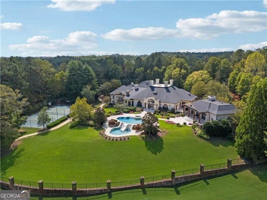 Extraordinary 20,000+ sq ft estate in the Hawks Ridge Golf Course community sits on 8 landscaped acres and features a European-inspired design with a private recording studio. With 8 bedrooms, 9 full baths, and 3 half baths, it offers a perfect blend of luxury interiors and resort-style outdoor living. Conveniently located, it's just 5 minutes from shopping/dining, 10 minutes to Milton, 45 minutes to Buckhead, or 15-20 minutes by helicopter. Cherokee County Regional Airport is only 15 minutes away, making Nashville just a 1-hour flight, offering incredible accessibility for any travel needs.  Upon arrival, the estate makes a grand statement with its security gate leading to a circular entry courtyard, offering easy access to the main home, studio, 5-car garages, and guest cottage. Inside, soaring ceilings, rich architectural details, and timeless sophistication await. The formal living room boasts vaulted ceilings with wood beams, expansive arched windows, and a grand limestone fireplace, while travertine floors and custom chandeliers elevate the elegant atmosphere, making it perfect for both intimate gatherings and large-scale entertaining. The recently remodeled gourmet kitchen is a chef's dream, featuring Taj Mahal Leather Quartzite countertops, a limestone range hood, and high-end Thermador and Subzero appliances. The light cabinetry, slate flooring, and grasscloth wallpaper create a refined and functional space, and the large island offers ample seating for casual dining, making this the heart of the home for family and friends. The nearly 3,000 sq ft main-level primary suite offers a serene retreat, with a Juliette balcony overlooking the pool, outdoor entertaining area, and golf course. The primary bath includes dual vanities, a steam shower, a soaking tub, and separate commodes. Two oversized walk-in closets, including a two-story custom closet, provide abundant storage, while the adjoining wood-paneled office/library adds function and elegance.  The outdoor living spaces are truly spectacular and include a resort-style pool with multiple levels, an elevated hot tub, and a central water slide. A travertine pool deck is surrounded by lush landscaping and vibrant flower beds, creating a picturesque and tranquil environment. For those who love to entertain, the property offers multiple outdoor kitchens, dining areas, fireplaces, and a private tennis and basketball court.  The terrace level is entertainment-focused, with a professional movie theater featuring fabric paneling, a hand-crafted custom bar, meticulously carved by a master carpenter, and overlooking a large game room and living room. Additional amenities on this level include a gym, massage room, craft room, and two ensuite guest bedrooms.  For music enthusiasts, the multi-million-dollar recording studio features a live room, control room, and vocal booth all floated and with Overly doors for superior acoustics, offering a world-class private space for music production.  The estate is completed with a two-bedroom and two-car garage guest house, providing privacy for visitors or extended family. The attention to detail extends throughout the property, from the balconies and terraces to the timeless finishes and breathtaking views of Hawks Ridge Golf Course.  Hawks Ridge Golf Club is a prestigious 18-hole private golf course designed by Bob Cupp. Spanning 550 acres of rolling hills and lush greenery, this 18-hole championship course combines natural beauty with challenging play. The course features undulating terrain, pristine water hazards, and scenic landscapes that offer diverse shot opportunities. Known for its bent-grass greens and the iconic waterfall at the fifteenth hole, Hawks Ridge provides a world-class golf experience in a serene, secluded environment. It is a non-equity, private club with a grand clubhouse, fine dining, locker rooms, and a helicopter pad for added convenience, set within an exclusive community.