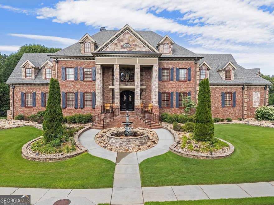 A magnificent estate where timeless architecture meets exceptional craftsmanship. Set on lush, rolling acres, this brick and stone masterpiece offers both grand entertaining spaces and serene outdoor retreats. A courtyard-style entry with a central fountain and dual staircases sets a dramatic tone. Inside, a soaring foyer with mirrored staircases leads to a formal living room featuring a stone fireplace and built-in bookcases, with direct access to a tranquil screened-in porch. The formal dining room impresses with coffered ceilings and intricate molding, ideal for elegant dinners. A hidden prep kitchen with double ovens, ice maker, and fridge adds convenience. The chef's kitchen boasts an oversized stone island with prep sink, 8-burner cooktop, double ovens, and wine storage, flowing into a sunny breakfast room and informal living area with a cozy fireplace.The main-level primary suite is a spacious, private retreat with a fireplace, morning bar, sitting area, and oversized windows. The spa-like bath features double vanities, a soaking tub, and a luxurious wraparound shower. Upstairs are four guest bedrooms with en-suite baths, connected by a dramatic open bridge hallway. A large storage closet and half bath add function. A stunning library-style study, adorned with rich wood paneling and custom murals, offers a refined escape. The terrace level is perfect for entertaining, with exposed beams, a cozy living room with fireplace, full bar and kitchenette, and lounge area with outdoor access. A half bath with mahogany paneling, large game room, and custom Georgia Bulldogs-themed home theater enhance the experience. A spacious gym and second half bath complete the level. Outside, a resort-style pool and hot tub create the ultimate retreat. The cabana features two grills, a microwave, counter space, and a fireplace. A koi pond adds tranquility. The carriage house sits above an oversized garage with space for large vehicles or a car collection. It offers a full kitchen, living and dining areas, and two private bedrooms with full baths-ideal for guests. Surrounding the home, manicured gardens and mature trees enhance the setting. A charming barn adds versatility, perfect for storage or a workshop, blending seamlessly into the estate's classic aesthetic.