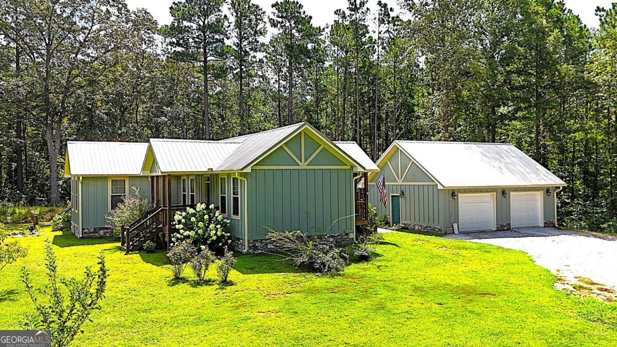 Custom Home on Acreage! The owner was inspired by Aerial Images of European Cathedrals and asked the designer to draw a house plan based off that image in her mind's eye....this beautiful home is the result of that inspiration! Enter the doorway from the detached garage and the Cathedral inspiration continues, wood and stone everywhere! Soaring Vaulted Ceilings of stained wood, stone fireplace, durable LVP flooring and tons of natural light bathe this space in warmth.! Open concept defined! Living, Cooking, and Dining all in this space, the huge custom-built island with salvaged wood top looks like it's been here 100+ years, but with a microwave oven built in! Gleaming stainless-steel appliances in this chef's kitchen, Corian counter tops with glass backsplash, stainless steel vent hood over the gas cooktop....this space is just begging for the family holidays where the conversations, cooking and laughter fill this space with the sounds of joy and love! At the end of this fellowship space, walk through the giant barn doors to enter the "quiet part" of the home! The hallway off the common area maintains the cross-like architectural design of the home, with the secondary bedrooms at opposite ends of the hall and the master suite just ahead! Enter this area into your own private sanctuary! The large master bathroom with soaking tub and enormous walk-in closet are just part of the incredible space....just through a second set of barn doors, is the private study or sitting room that makes you want to curl up with a warm blanket and a great book to unwind! With tons of windows and a glass door heading out to your private back deck, this space might be the best spot in the house to seek a little serenity and solitude. The current owner uses the adjoining room as an art room but put up a door and a closet door and it is the 3rd bedroom. At the other end of the hall is the other bedroom and full bath which feels as though it's on its own "wing" of the house, again with high ceilings and tons of windows this bedroom is spacious yet private and cozy! Step out the doors in literally every direction and the surroundings are as inspiring as the stuning home! Tucked into a 6.5 acre wooded parcel at the end of the winding gravel path this place is a hidden little piece of heaven! The circular driveway is anchored by a great 2-car detached garage or workshop, with the interior walls and ceilings wrapped in durable metal, cabinets with a sink, and it even has a bathroom! Truly a "one of a kind", the property has great details that may not be immediately noticable, such as a small koi pond, fruit trees, specimen plantings, and multiple porches and nooks, outdoor areas, mature pines all of which together make this home feel like it has been here for decades but with all of the modern conveniences and efficiencies of a home that is less than 6 years old! Ideal home for the retirees wanting to downsize to single floor living, or perfect for the young family that is looking to escape the subdivision lifestyle and discover a new way to LIVE!!!