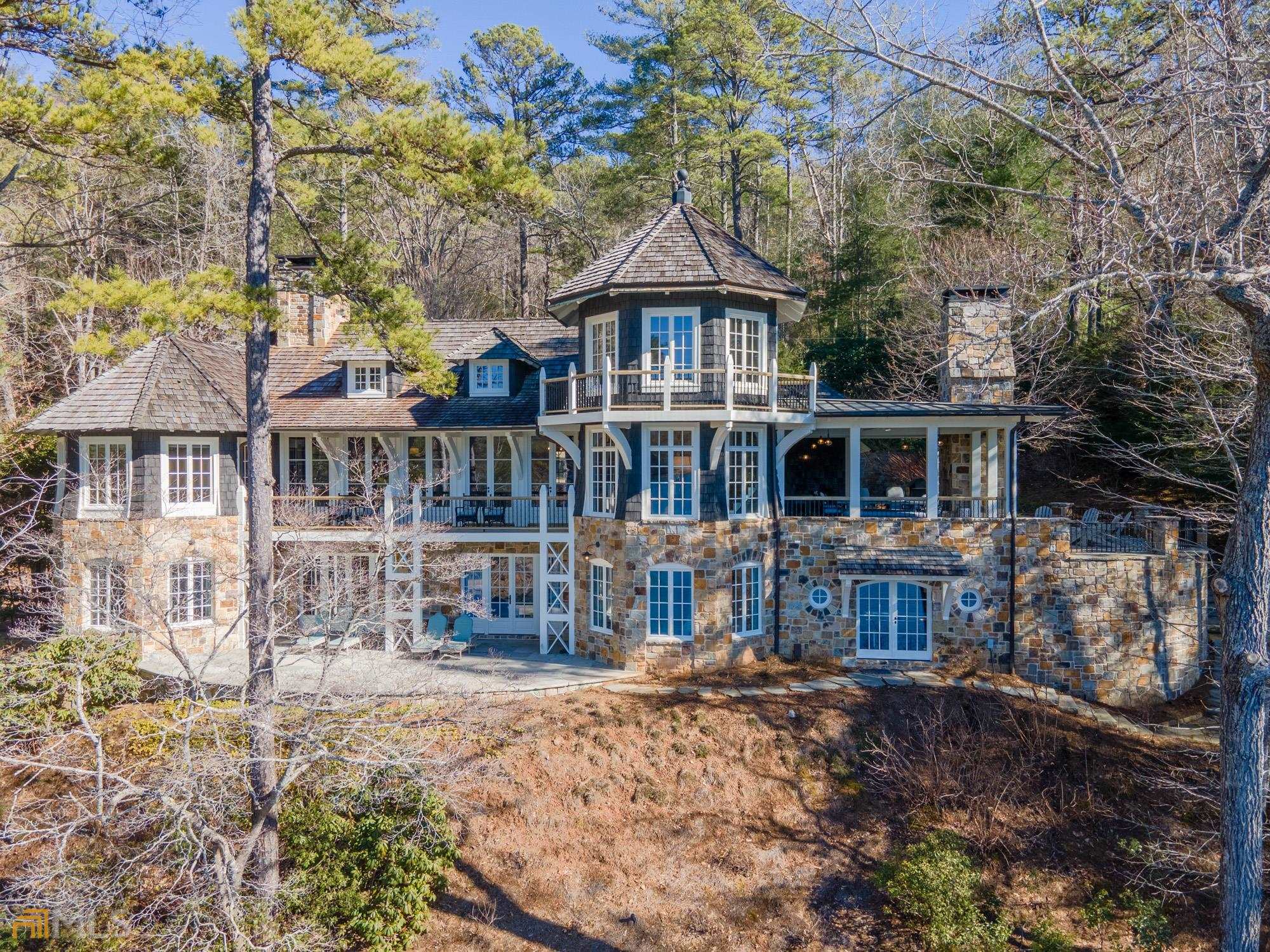 Designed by celebrated architect Yong Pak and built by Chris Clay of Clay Contracting, this impressive 5 bedroom, 5 full bath and 2 half bath Lake Burton residence combines exquisite craftsmanship with coveted mountain sunset views. The great room features a vaulted barnwood ceiling and stone fireplace flanked by built-in bookcases. A generous dining area and wall of French doors lead to a lakeside rocking chair porch. The professional chef's kitchen boasts Calacatta marble countertops with Wolf and Sub-zero appliances, a wet bar with icemaker, beverage cooler and stem wear dishwasher, walk-in pantry and dining nook. French doors from the kitchen lead to a covered lakeside patio with plenty of space for dining, lounging and grilling around the double sided outdoor fireplace while enjoying long range mountain and sunset views. The main-floor owner's suite comes complete with a fireplace, lake views, and a sumptuous spa-like bath with heated marble flooring, freestanding tub and steam shower. A home office, laundry room and 2 powder rooms complete the main floor, along with access to a crow's nest reading room/office overlooking the lake. On the terrace level, a family room with a stone fireplace includes a wall of built-in bunk beds with access to a full bath. A second terrace level family room and game area is equipped with a wet bar with sub zero refrigerator/freezer column and ice maker. French doors open to a pathway leading to the 2-stall boathouse. Two private guest bedrooms feature en-suite baths and French doors leading to a lakeside patio. Two additional guest bedrooms share a spacious bathroom, one with access to a lakeside patio.