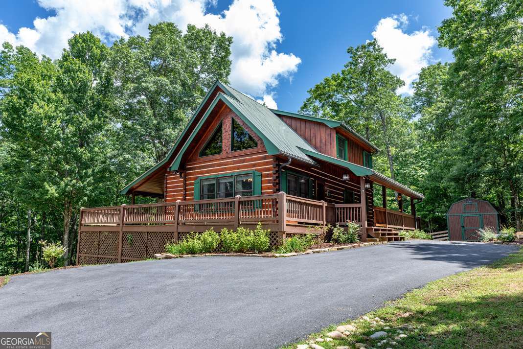 Set in a peaceful mountain landscape with mature trees and thoughtfully designed outdoor spaces, this beautifully updated log cabin offers the perfect balance of rustic charm and everyday comfort. The cozy great room features large windows that flood the space with natural light, soaring vaulted ceilings, rich tongue-and-groove walls, and a gas fireplace that creates a warm, inviting atmosphere. The open floor plan includes a well-equipped kitchen with a 5-burner gas stove, breakfast bar, and dining area, ideal for hosting friends or enjoying quiet evenings at home. The main-level bedroom opens to the back deck and connects to a full bath with a laundry closet, while the private loft suite offers a spa-inspired bath with soaking tub, double vanities, separate shower, and its own covered balcony. The finished terrace level includes a spacious recreation area, second gas fireplace, full bath, bedroom, and laundry room. Outdoor living is a highlight, with a wraparound porch and swing, a terraced garden seating area, and a stunning fire pit perfect for gathering under the stars. With a large barn-style outbuilding and convenient access to both Blairsville and Blue Ridge, this mountain retreat delivers timeless style, modern comfort, and a true sense of home.