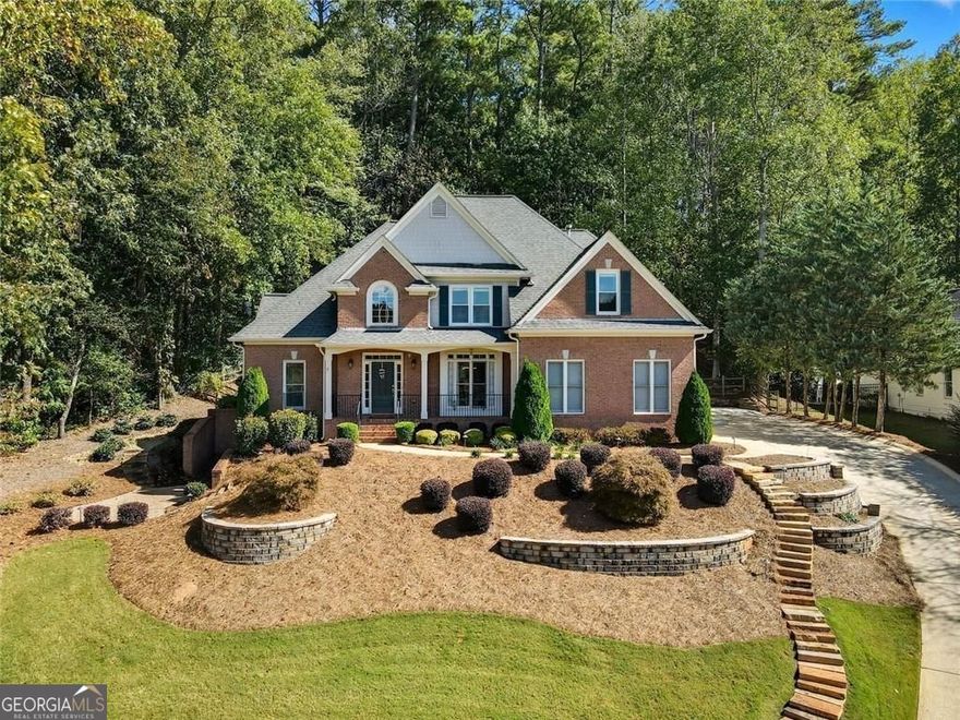 A Rare Find in Bradshaw Farm: Primary Suite on Main Plus Outdoor Living You'll Love  Set on a professionally landscaped lot in one of Woodstock's most sought-after communities, this five-bedroom, four-bath home pairs timeless brick architecture with thoughtful upgrades inside and out. A wide front porch with brick steps and stately columns welcomes you home, while terraced stone walls and manicured landscaping enhance the curb appeal.  Inside, the main level offers both functionality and comfort with a spacious primary suite featuring a walk-in closet and an oversized bathroom with separate vanities, a soaking tub, and a walk-in shower. An additional bedroom and full bath on the main level offers flexible space for guests, aging-in-place needs, or a quiet home office.  The heart of the home, the two-story great room, boasts a wall of arched windows and a fireplace that draws the eye up to the soaring ceiling. The kitchen is open and bright, outfitted with white cabinetry, granite countertops, stainless steel appliances, and a breakfast bar overlooking the screened porch and deck.  Step from the kitchen into a vaulted screened-in porch with exposed beams, then out to a freshly stained deck with room to grill, dine, and unwind. The fenced backyard is tree-lined for privacy with space to garden or play.  Upstairs, you'll find three generously sized bedrooms and dual entry bathroom. The finished terrace level extends your living space with multiple recreation areas, built-ins, a full bath, and a convenient kitchenette perfect for hosting, hobbies, or multigenerational living.  Enjoy all the perks of Bradshaw Farm living including golf, pools, tennis, pickleball, volleyball, clubhouse, and more just minutes from vibrant Downtown Woodstock, top-rated schools, and everyday conveniences.