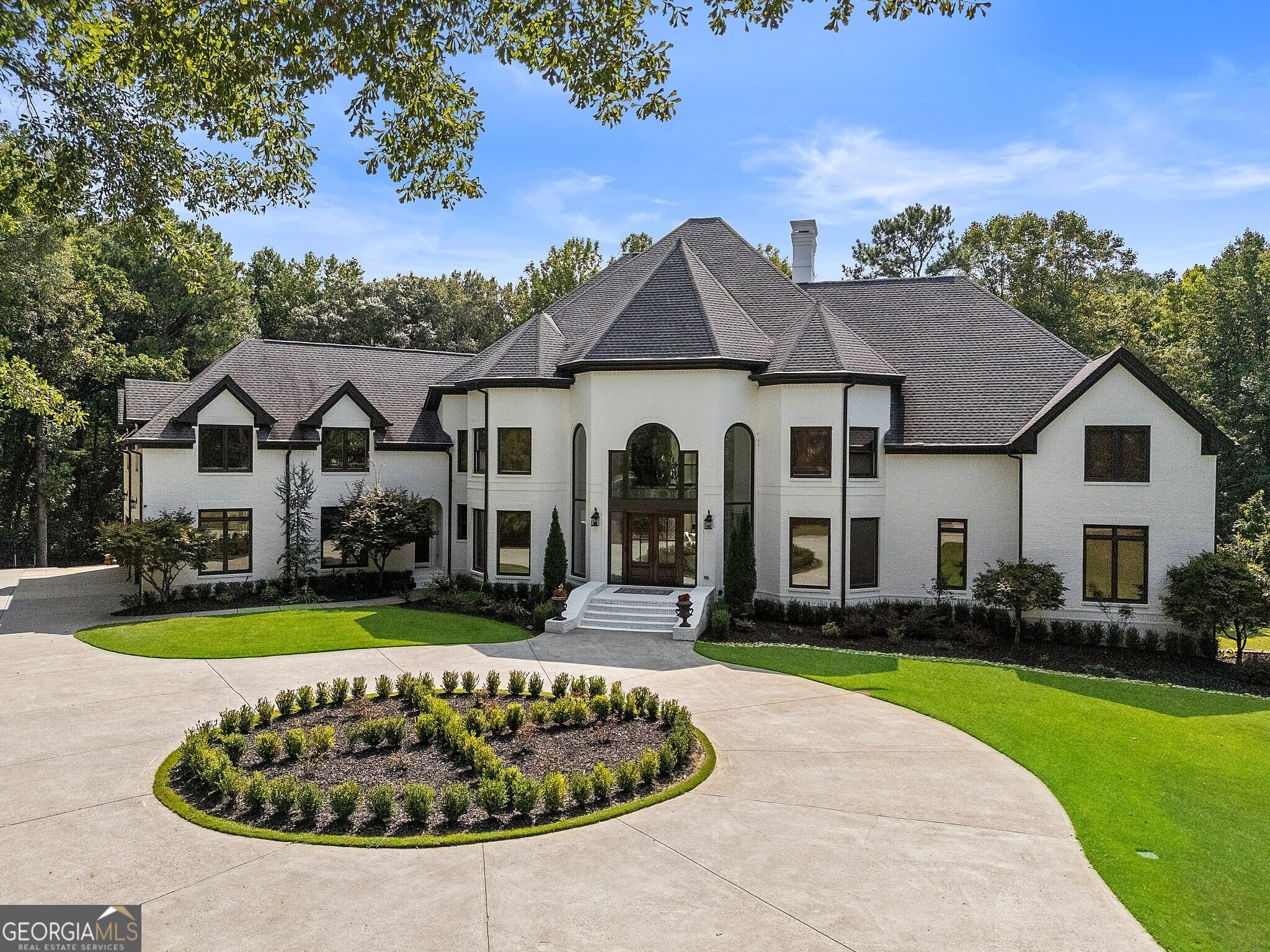 As you follow the long, private drive, you're immediately captivated by the grandeur of this Montclair Estate. Nestled on an expansive, beautifully landscaped property, this exquisite home commands attention from the moment you arrive. Upon entering, you're greeted by soaring ceilings and a striking glass balcony above, offering an immediate sense of openness and sophistication. To the right of the grand foyer, a refined office filled with natural light provides an inspiring space for work. To the left, the elegant dining room features a beautiful bay window that fills the space in soft light-perfect for hosting formal dinners. Beyond the dining room, a meticulously designed built-in aquarium captures attention, flanked by a modern wine cooler and wet bar. The formal living room is the focal point, featuring soaring coffered ceilings and a magnificent stone fireplace that anchors the space. The large panoramic windows overlooking the deck invite an abundance of natural light, creating an inviting ambiance throughout the main level. This sophisticated layout flows seamlessly into the heart of the home: a gourmet kitchen. At its center, a sprawling marble island offers ample seating for casual meals or entertaining. A herringbone-patterned backsplash adds a refined touch, while a large farmhouse sink, warming drawer, and high-end six-burner gas stove cater to all your cooking needs. Double ovens and a strategically placed microwave ensure perfect meal preparation. The kitchen transitions gracefully into a spacious open-concept living area, where a charming breakfast nook sits adjacent to a cozy sitting area centered around a beautifully designed fireplace. This space effortlessly accommodates a variety of social occasions. An oversized pantry with custom-built shelving offers practical storage solutions, while a generously sized laundry room across the hall features additional built-ins and a convenient sink. Located on the main floor, the tranquil primary suite awaits. This luxurious retreat features a cozy fireplace and oversized windows that blend comfort with sophistication. A dedicated sitting area, complete with a morning kitchen, provides a peaceful corner for relaxation. The spa-inspired primary bath features a lavish soaking tub and an oversized walk-in shower for a rejuvenating experience. A double vanity with custom cabinetry and two expansive walk-in closets-complete with a central island-offer exceptional space and organization. Upstairs, four generously sized guest bedrooms, each with a luxurious full bath featuring modern fixtures and ample storage. At the end of the hallway, a bright and versatile bonus room serves as a playroom or additional office space. A conveniently located laundry chute adds a thoughtful touch, connecting directly to the main laundry room below. The terrace level features additional living spaces, from a lounge to a game room; this is an entertainer's paradise. You'll find a custom home theatre with elevated seating and cinematic lighting, a spacious home gym, a massage room and more. This level also features a fully equipped second kitchen and bar area, complete with stovetops, a mini fridge, microwave, ice maker, sink, and built-in shelving-perfect for entertaining. Two additional bedrooms share a well-appointed Jack-and-Jill bathroom, ideal for guests. The thoughtfully landscaped grounds create a peaceful and picturesque setting. A charming porch and patio space invite you to relax. At the heart of this outdoor oasis is a stunning resort-style pool with a luxurious hot tub, as well as a grill and prep area. The flat, spacious yard provides ample room. Located in prestigious Johns Creek, adjacent to the Chattahoochee National Forest and River, this estate blends architectural grandeur with everyday functionality. It offers a lifestyle defined by elegance, comfort, and connection-luxury living at its finest.