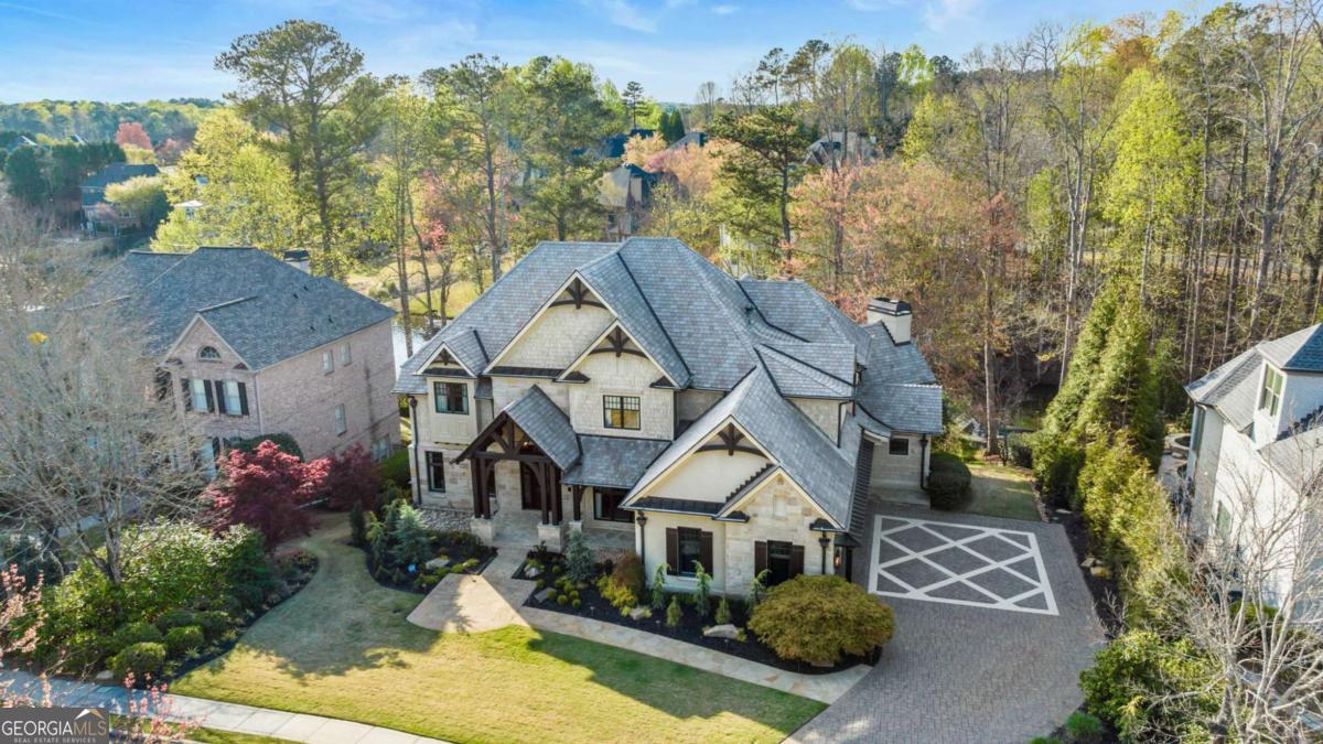 Welcome to an extraordinary residence in the prestigious Windward community, where refined craftsmanship meets modern living. This extensively renovated lakefront home has an effective age of just six years, thanks to a top-to-bottom transformation using only the highest-quality materials and finishes. Step inside through custom oak front doors into a grand two-story foyer, where a curved limestone stairway, designer chandelier, and wide-plank walnut flooring set the tone for the rest of the home. Every inch of this property has been thoughtfully curated-from the five Francois & Co. designer fireplaces to the rich limestone and Carrara marble tile, custom lighting, and home-wide audio systems. The two-story great room features a limestone fireplace and coffered ceiling with integrated lighting, leading to a bright sunroom and upper-level decks that capture stunning Lake Windward views. The kitchen is a culinary masterpiece, complete with leathered granite counters, state-of-the-art appliances, and a hidden catering kitchen/scullery with its own built-in smoker and grill system-perfect for entertaining. Upstairs, the primary suite is a true retreat: a tray-ceilinged bedroom with fireplace, a spa-inspired bathroom with heated Carrara marble floors, a glass-enclosed steam shower with eight jets, and two expansive designer dressing rooms, each with custom cabinetry and vanities. The terrace level is a full entertainment destination, boasting a bar with crystal tile, a home theater, a game room with herringbone plank floors, and a guest suite with spa bath and separate fitness room. Accordion-style glass doors open to a covered porch with Phantom screens, a stone patio with built-in firepit, and curved stairs leading to your private dock. Exterior highlights include: DaVinci slate tile roof (50-year warranty) Windsor bronze-clad casement windows Professional landscaping and stone pathways Upper and lower slate-tiled decks Soft water filtration system Mosquito misting system Two tankless water heaters & zoned thermostats Located in the highly desirable Windward neighborhood, residents enjoy resort-style amenities such as a private lake, sports park, tennis and pickleball courts, walking trails, a golf course, and social clubs. Just minutes from GA-400, Avalon, and Halcyon, this home offers the perfect blend of peaceful lakefront living and modern luxury convenience.