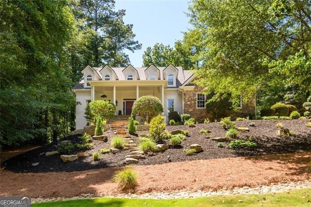 Park-Like Retreat in the Heart of Johns Creek! Step into timeless elegance with this exceptional 5,000+ sq ft estate nestled on over an acre of beautifully landscaped grounds in one of Johns Creek's most sought-after neighborhoods-known for its safety, top schools, and vibrant lifestyle. Set on a raised elevation, the home boasts breathtaking curb appeal, with custom fully irrigated landscaping, landscape lighting, and a wide front porch that welcomes you into a world of warmth, luxury, and function. Inside, soaring ceilings over 20 feet high in the great room frame a mahogany wall of windows that draw your eye to the stone and timber veranda overlooking the spectacular outdoor setting. The open floor plan with hardwood floors offers effortless flow, yet maintains a cozy, inviting atmosphere perfect for both grand entertaining and intimate evenings. At the heart of the home is a chef's dream kitchen-commercial-grade appliances, copper farmhouse sinks, custom cabinetry, and expansive prep space for everything from small dinners to large-scale entertaining. A large walk-in pantry with laundry hookups provides one-level living flexibility, complementing the spacious main-level primary suite, complete with a sitting area, custom closet cabinetry, and luxurious bath. Upstairs, you'll find three generously sized bedrooms, two full baths, a charming playroom or art studio, and a full laundry room. The finished terrace level offers incredible versatility with a private in-law suite, full kitchen area, gym, workshop, theater, and game room-perfect for multigenerational living or serious entertaining. Step outside to your private sanctuary: a sprawling veranda with stone flooring, pine tongue-and-groove ceilings, hand-carved mortise and tenon framing, and wood trusses. The outdoor kitchen features a Big Green Egg, gas grill, fridge, ice maker, expansive serving/dining counter and custom lighting-ideal for unforgettable gatherings. Stroll winding paths through the backyard, relax by the self-draining, large stone fire pit surrounded by natural boulder seating, or enjoy the magic of custom lighting under the canopy of stars and trees. Every detail has been meticulously maintained-fresh interior and exterior paint, updated systems, whole-house on-demand water heating, and a new roof in 2023. This incredible home is truly move-in ready. Located in Johns Creek-named the #1 Best Place to Live in the U.S. by U.S. News & World Report in 2025-this home is just minutes from top-ranked public and private schools, the Atlanta Athletic Club, premier golf, dining, parks, river access, and theaters. This is not just a home-it's a lifestyle. *Source: U.S. News & World Report, "Best Places to Live in the U.S.," 2025-2026*