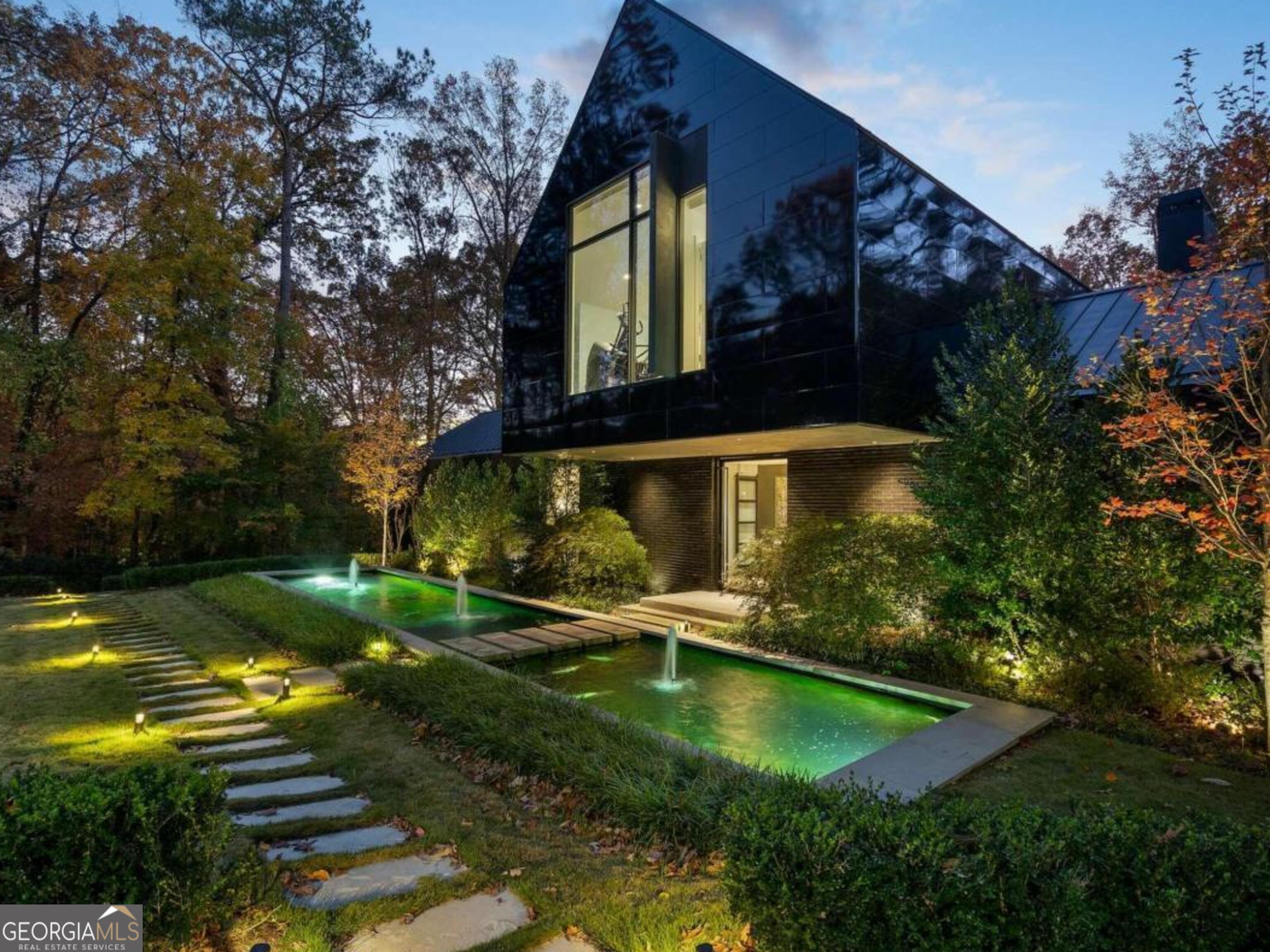 This exceptional Buckhead residence, thoughtfully designed by renowned architect Robert Tretsch III of Harrison Design, designed specifically for the lot (1.19 acres) that is also adjacent to protected land, Standing Fort Peachtree. The evolving landscape and koi ponds further enhance the design of this residence.  ADCO Builders and Harrison Design completed this residence in 2020 specifically as the Decorator Showhouse to commemorate the Atlanta Symphony's 75th Anniversary.  The exterior is Meridian brick and the black reflective wall panels, the first in the U.S. are Nichiha Miraia by Legendary Exteriors.  Upon arrival, guests are greeted by a striking water feature and koi pond and La Cantina glass pivot door. Stepping inside, the dramatic design unfolds to three stories of Windsor commercial-grade glass and steel frame with breathtaking views of the natural beauty of the property. The home's architecture is expertly oriented to capture optimal east-to-west exposure, flooding the interiors with natural light at every turn. The custom designed kitchen by Design Galleria features a 15 foot island in Temmer marble, custom cabinets by Kingdom, Wolf ovens and steam oven, Sub Zero and walk in hidden pantry.  Open to the family room with fireplace and doors out to a covered private patio. The dramatic dining room appears to float over the living room capturing views of the pool and property. The primary bedroom suite has floor to ceiling glass overlooking the pool. The bedroom features separate dressing rooms, a dreamy bath and quiet study with morning kitchen and an outdoor patio that overlooks the pool.  The expansive lower level is an entertainer's dream, featuring the main living room overlooking the 65 foot pool and featuring two fireplaces. The bar, theater and billiards are perfect for entertaining.  Two guest suites open directly to the pool area.  The upper level includes two additional bedroom suites and a second laundry room. Built with the latest energy-efficient systems, this home is equipped with Lutron controlled lighting, elevator and advanced technology for ultimate comfort and convenience. Nestled in the exclusive Paces Estate neighborhood-Buckhead's best-kept secret-this home enjoys a serene, tree-lined setting with minimum one-acre lot sizes, preserving both privacy and natural beauty. Conveniently located near Buckhead's top shopping, dining, and entertainment, and with easy access to the airport, this residence offers the perfect combination of luxury, tranquility, and proximity to city amenities.