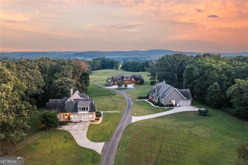 Nestled in picturesque Gilmer County, this sprawling 122  acre cattle farm in Ellijay boasts two beautiful homes, peaceful rolling hill pasture, a meandering creek and pockets of dense hardwood thickets. The three-bedroom, two-and three-half-bathroom main house boasts an inviting covered front porch that opens to a two-story foyer. The gourmet kitchen includes rich wood cabinetry, granite countertops, stainless steel appliances and a large island with a breakfast bar, which is all open to the dining area and has a vaulted living room. Floor-to-ceiling windows frame the property's stunning views, while a wood-lined cathedral ceiling and a stone fireplace flanked by built-ins add warmth to this large, welcoming keeping room. Two sets of French doors open to the covered porch, complete with an outdoor fireplace, a TV hookup, access to the screened porch and a half pool bathroom. Unwind in the spacious primary suite, which boasts a beamed cathedral ceiling, porch access, dual walk-in closets and a luxurious en suite bathroom with separate vanities, a freestanding soaking bathtub and a shower with multiple showerheads. Two additional main-level bedrooms are connected by a Jack-and-Jill bathroom. Completing the main level are an enormous laundry room with extensive cabinetry and storage, a half bathroom and access to the three-car garage. Upstairs, enjoy a bonus loft space with a half bathroom and plenty of room for a sitting area, games or an additional sleeping area. Outside, soak up the sun by the large saltwater pool, a spa with a waterfall feature and a diving board- all fenced and overlooking the verdant grazing grounds. The second home on the property sits on 3 of the 122 acres, and offers incredible living space with three bedrooms and three bathrooms. Enter from the covered front porch into the open floor plan layout. The large family room features a stone fireplace, a cathedral ceiling and access to the fireside rear screened porch. The adjoining dining space flows directly into the kitchen, which includes an island with seating, granite countertops, stainless steel appliances and timeless neutral cabinetry.  The pristine hardwood floors continue into the sleeping quarters, which include a tranquil primary suite with an en suite bathroom and two en suite guest rooms. The laundry room provides a utility sink, built-in storage and a drop-zone area to keep everything tidy. Upstairs, a large bonus room is perfect for a recreation room, office or additional bedroom. A two-car garage on the main level completes this immaculate home. The property includes various outbuildings/pole barns for hay and farm equipment storage, as well as a cattle barn and chicken shed. Located in the foothills of the North Georgia Mountains and just seven miles from downtown Ellijay, enjoy restaurants, wineries and charming retail stores, as well as Carter's lake just minutes from this breathtaking property! Experience the beauty, serenity and opportunity that await in beautiful Ellijay!