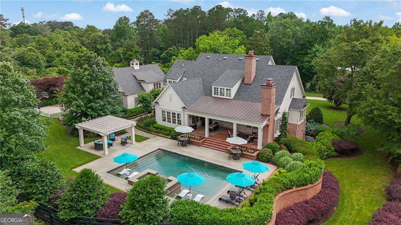 Experience refined Southern living in this luxury gated custom built farmhouse by renowned builders Smith and Kennedy. Perfectly positioned on 1.6 beautifully landscaped acres in the heart of Roswell, this extraordinary six bedroom, six full baths and two half bath estate offers a seamless blend of timeless craftsmanship and modern sophistication. From the moment you arrive, the charm is undeniable. A gracious rocking chair front porch with ceiling fans invites you to unwind and take in the tranquil surroundings. Step inside to find an open concept floorplan adorned with rich hardwood floors, shiplap ceilings, and exquisite designer chandeliers. The brick walled dining room, framed by an exposed beam ceiling and dramatic lighting, sets the stage for unforgettable gatherings. The heart of the home is the chef inspired kitchen, featuring quartz countertops, a generous center island, and top of the line appliances designed for both beauty and performance. The main level owners suite is a private sanctuary with a spa caliber bath complete with double vanities, a soaking tub, oversized shower, and a custom walk in closet tailored to perfection. Function meets elegance in the thoughtfully designed laundry and mud room, offering a built in sink and dedicated dog bath. The terrace level is an entertainer's dream with a full guest suite, expansive living area, billiard room, home gym, and a well equipped kitchenette - ideal for extended guests or multigenerational living. Step outside to enjoy resort style amenities including a covered rear porch, pergola, and an inground saltwater pool - a private oasis for relaxation and entertaining year round. Ideally located just moments from Roswell's vibrant Canton Street, top tier shopping, dining, parks, and some of the area's most prestigious private schools including Fulton Academy and Fellowship Christian School. This is more than a home - it is a lifestyle of beauty, comfort, and distinction.
